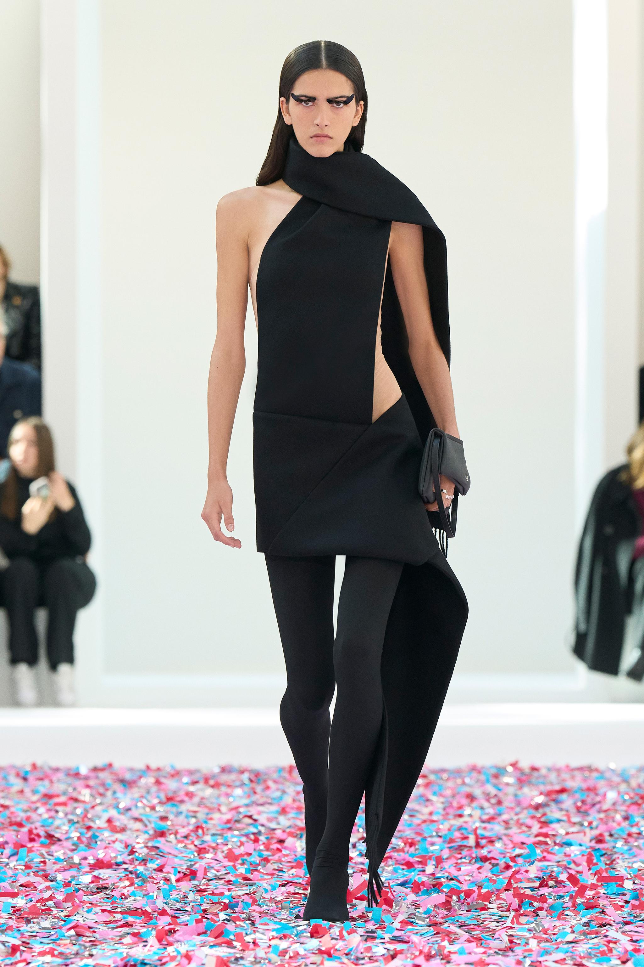 Elegant black couture dress with asymmetrical design, showcased on a runway by Courrèges.