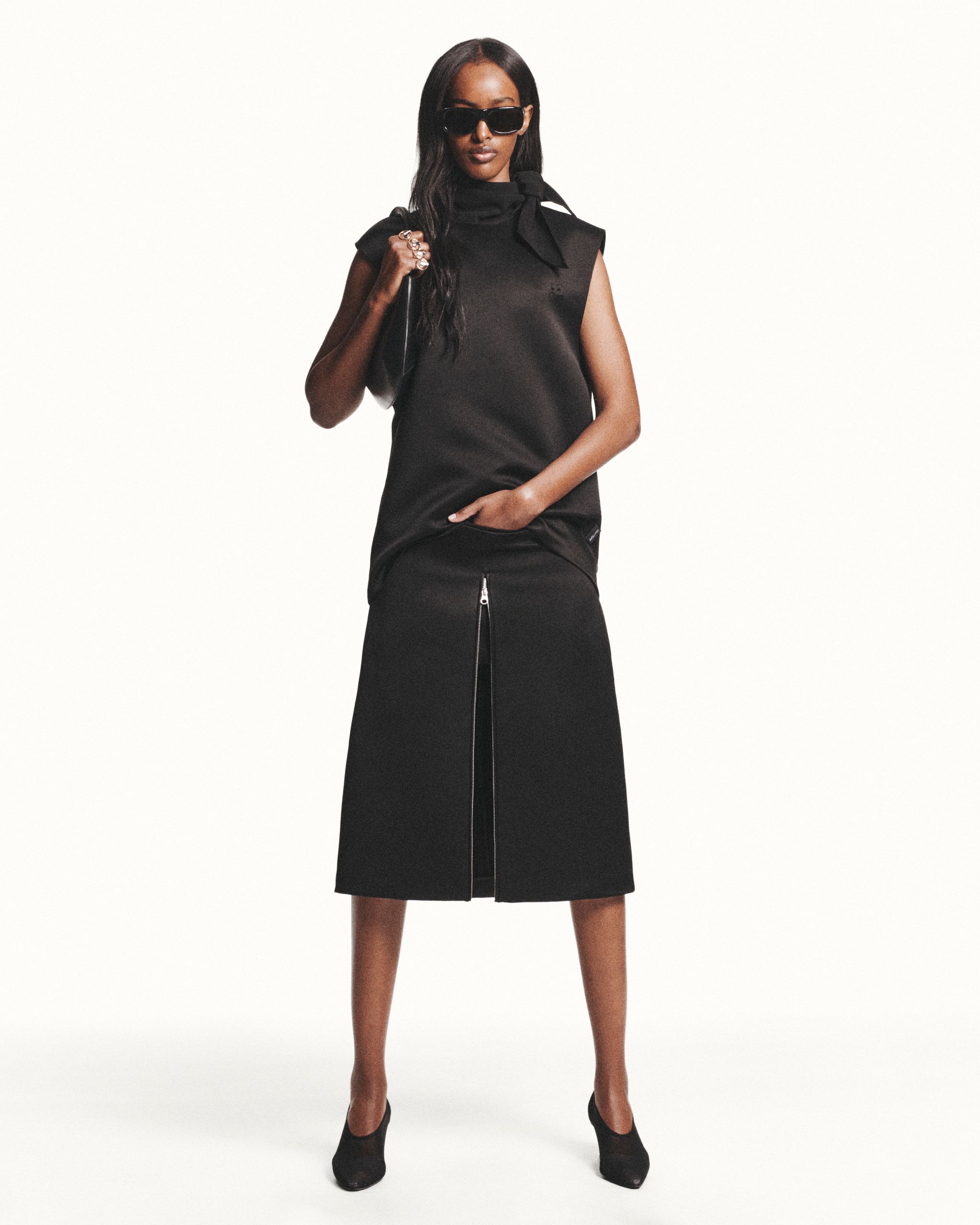 Elegant black fashion ensemble featuring a sleeveless top, midi skirt, and chic accessories for Courrèges.