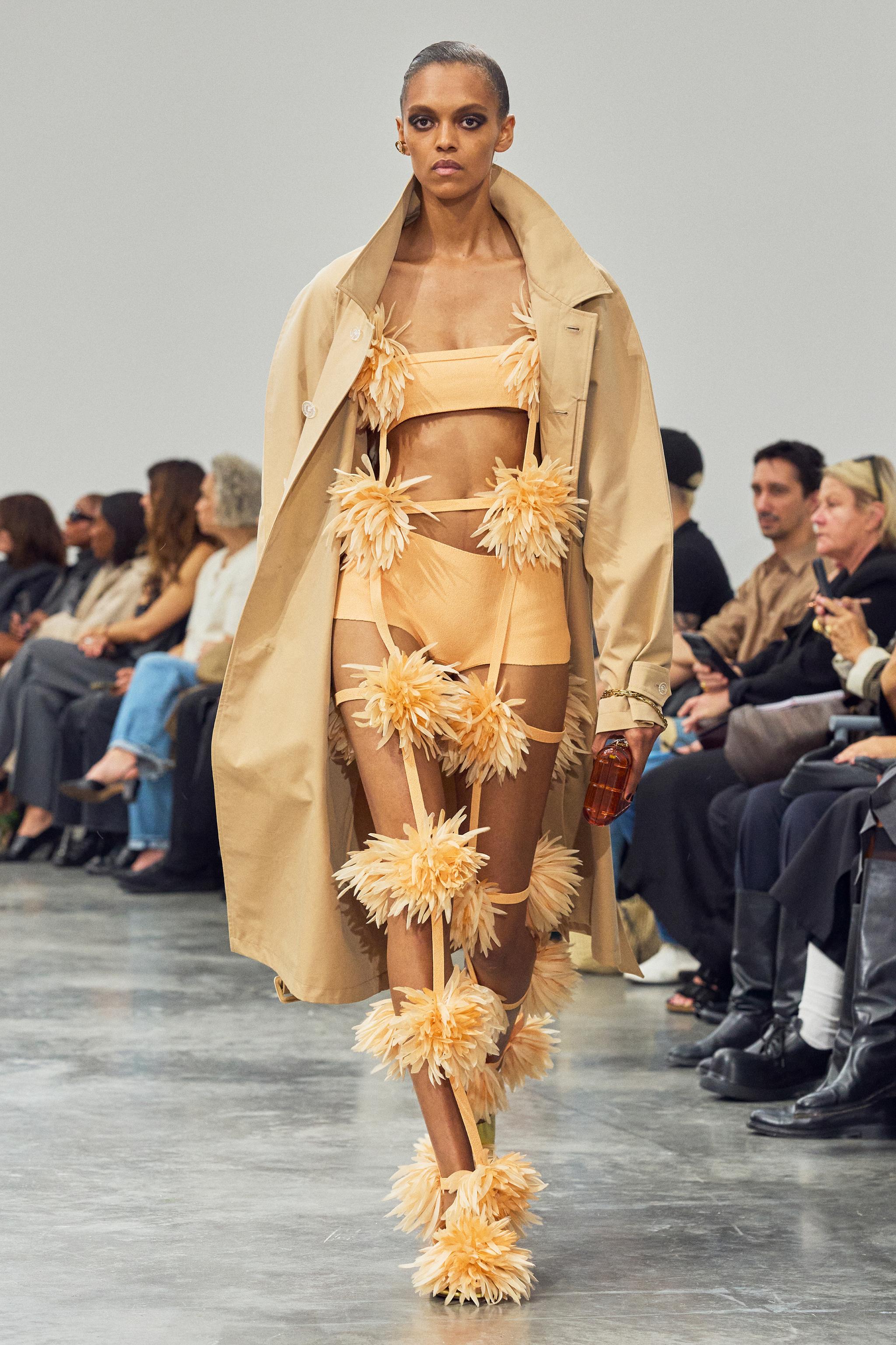 Fashion runway model wearing Courrèges avant-garde floral-inspired ensemble, beige coat and accessories.