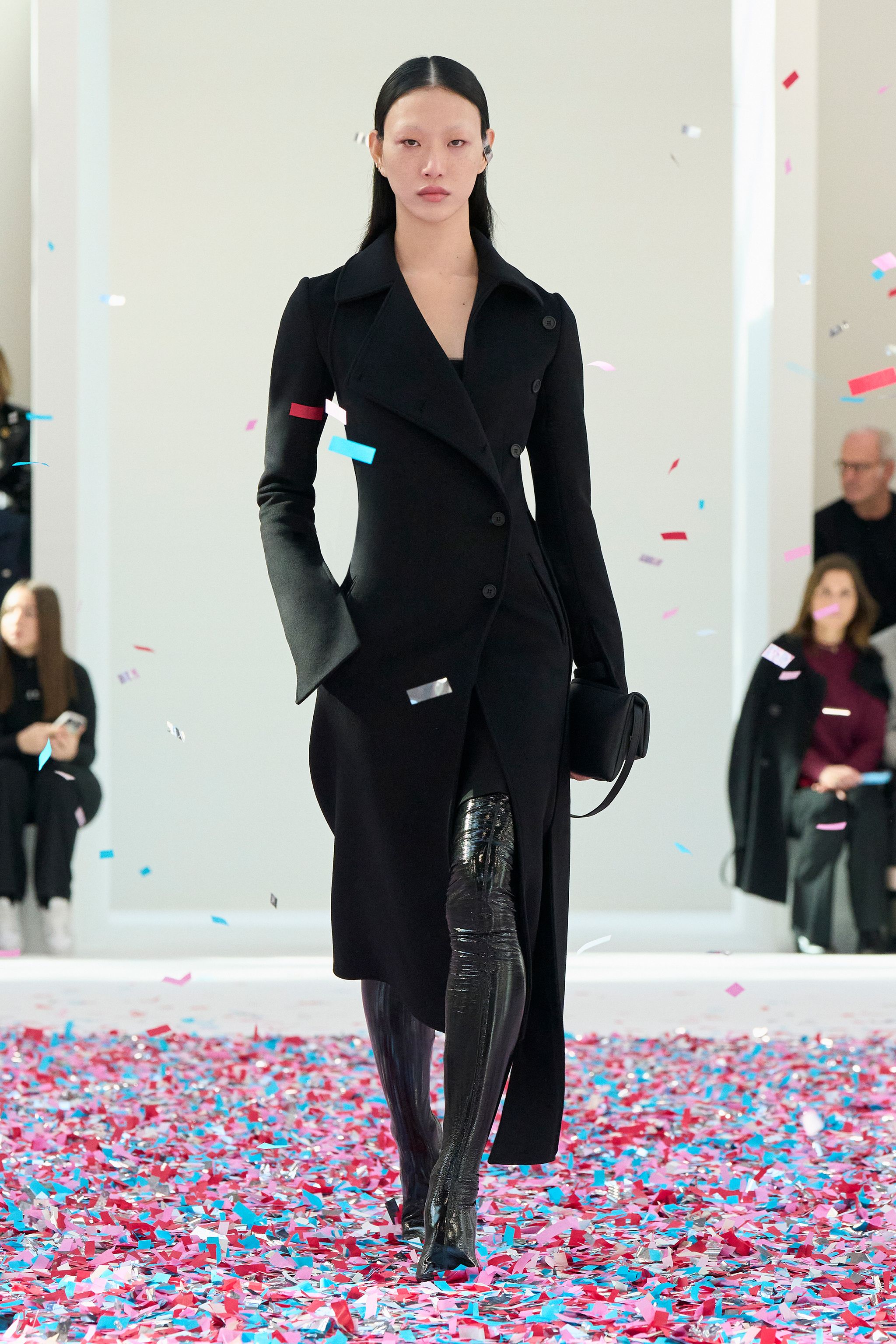 Elegant model wearing a black Courrèges coat on runway with colorful confetti, for ecommerce.