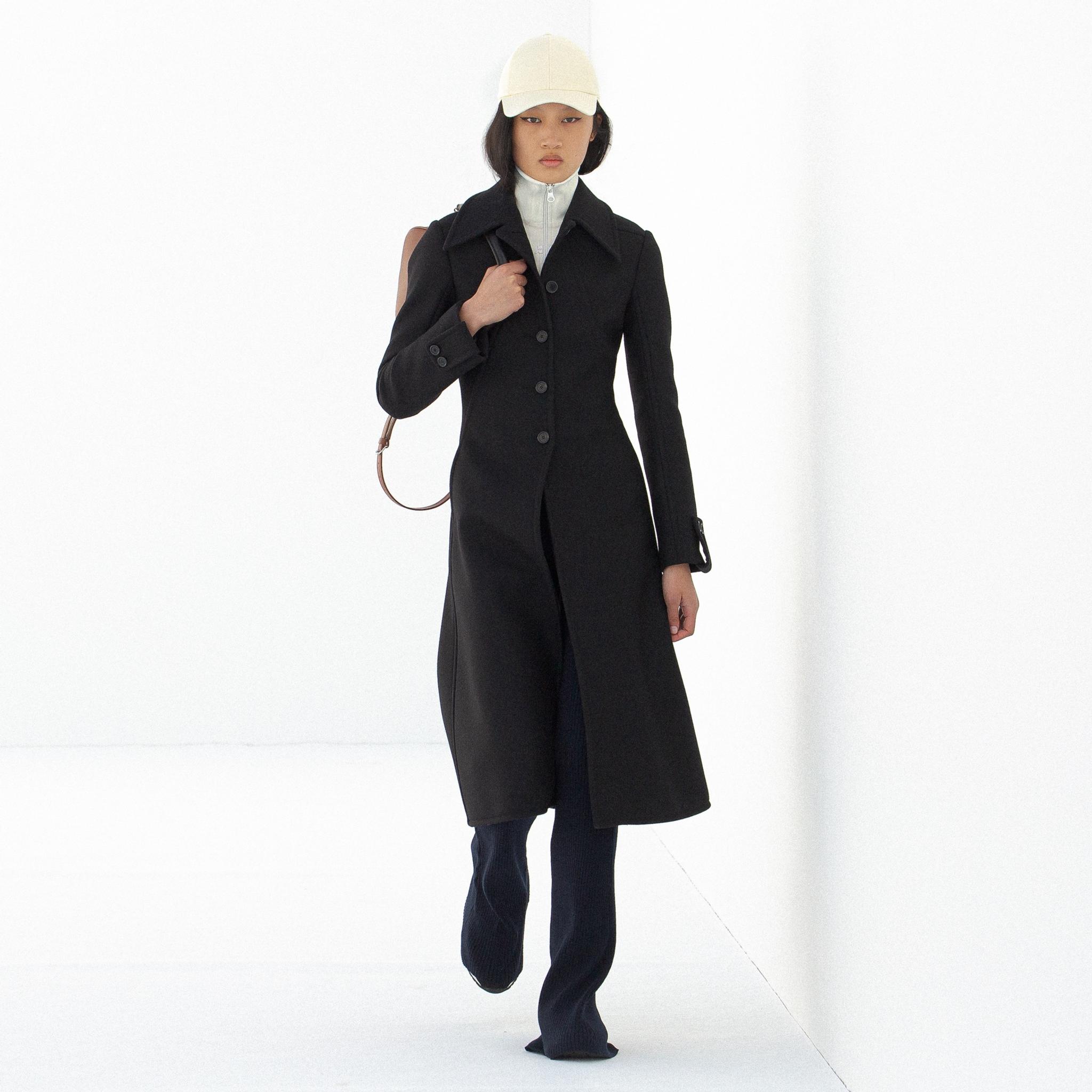 Manteau noir élégant de Courrèges, présenté sur un mannequin dans un cadre minimaliste.