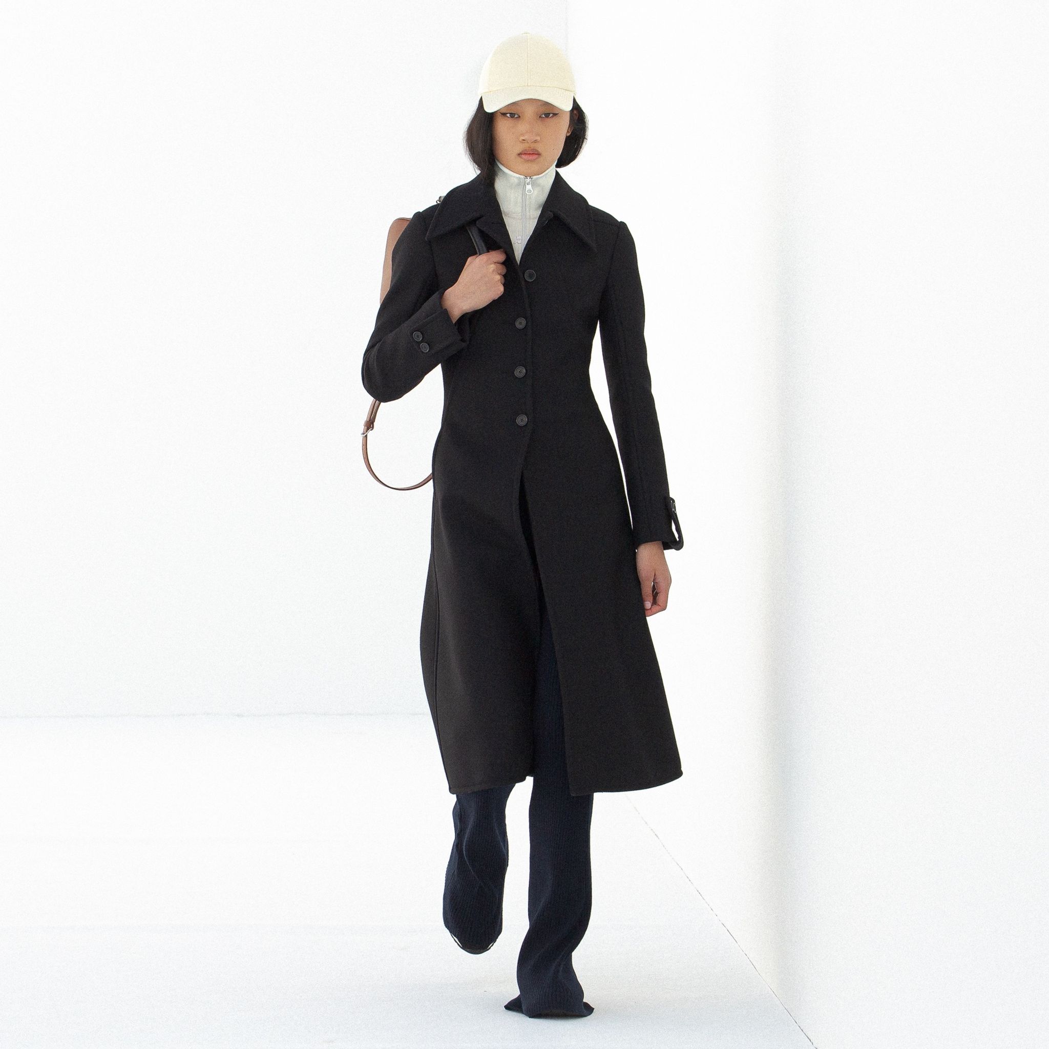 Elegant black coat from Courrèges, showcased on a fashion model in a minimalistic setting.