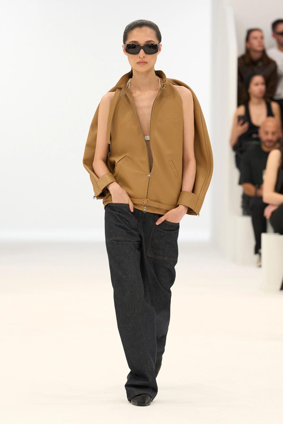 Elegant model showcasing Courrèges fashion with a tan vest, black jeans, and stylish accessories.