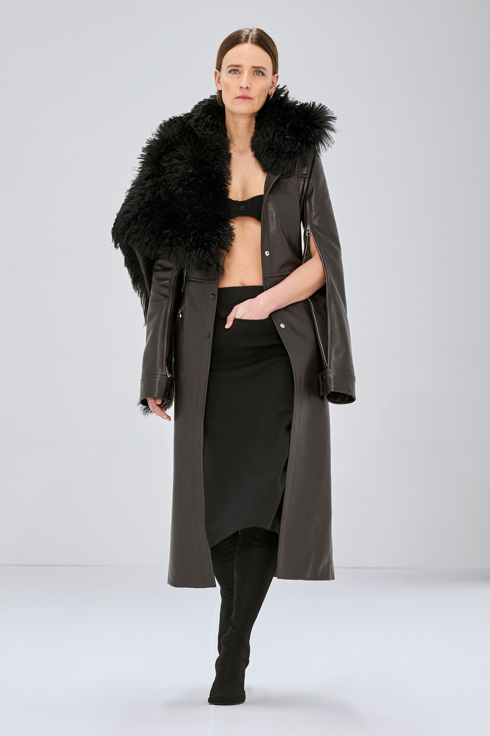 Elegant black leather dress with a faux fur stole, styled for Courrèges fashion on a runway.