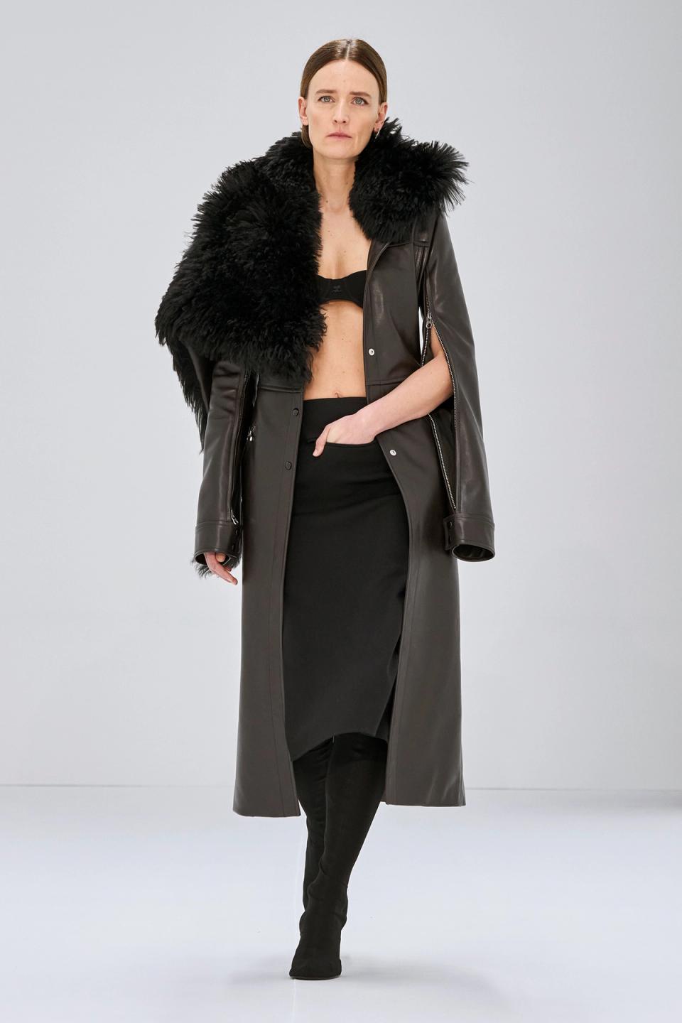 Elegant black leather dress with a faux fur stole, styled for Courrèges fashion on a runway.