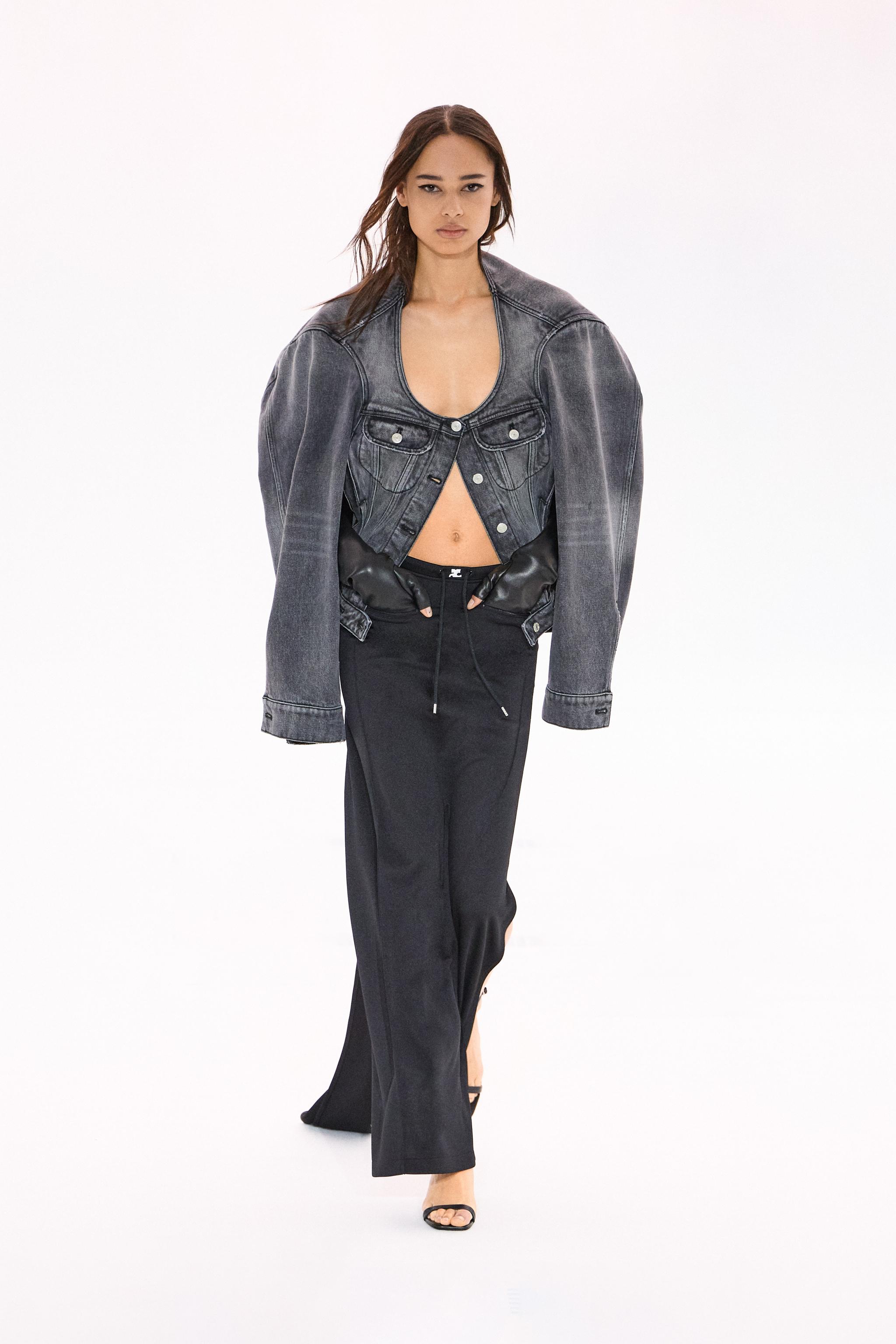 Fashion model wearing a black denim jacket and wide-leg black trousers on a white background.