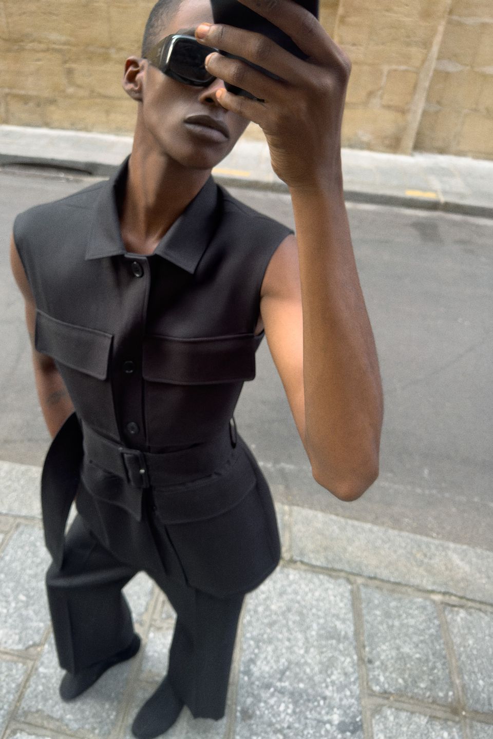 Elegant black sleeveless outfit by Courrèges, featuring stylish sunglasses, on an urban street.