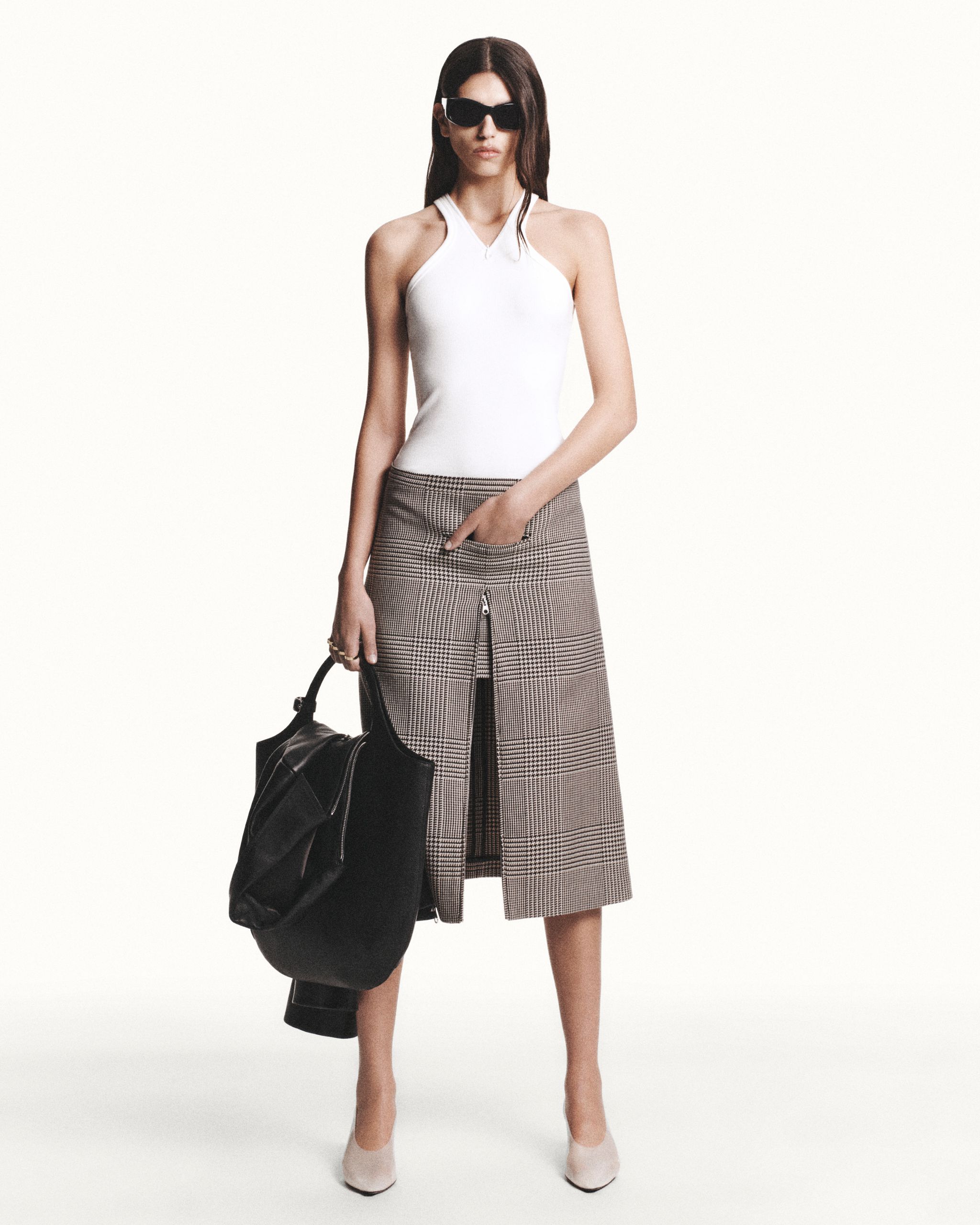 Elegant model in Courrèges fashion brand outfit, white top, checkered skirt, black bag, sunglasses.