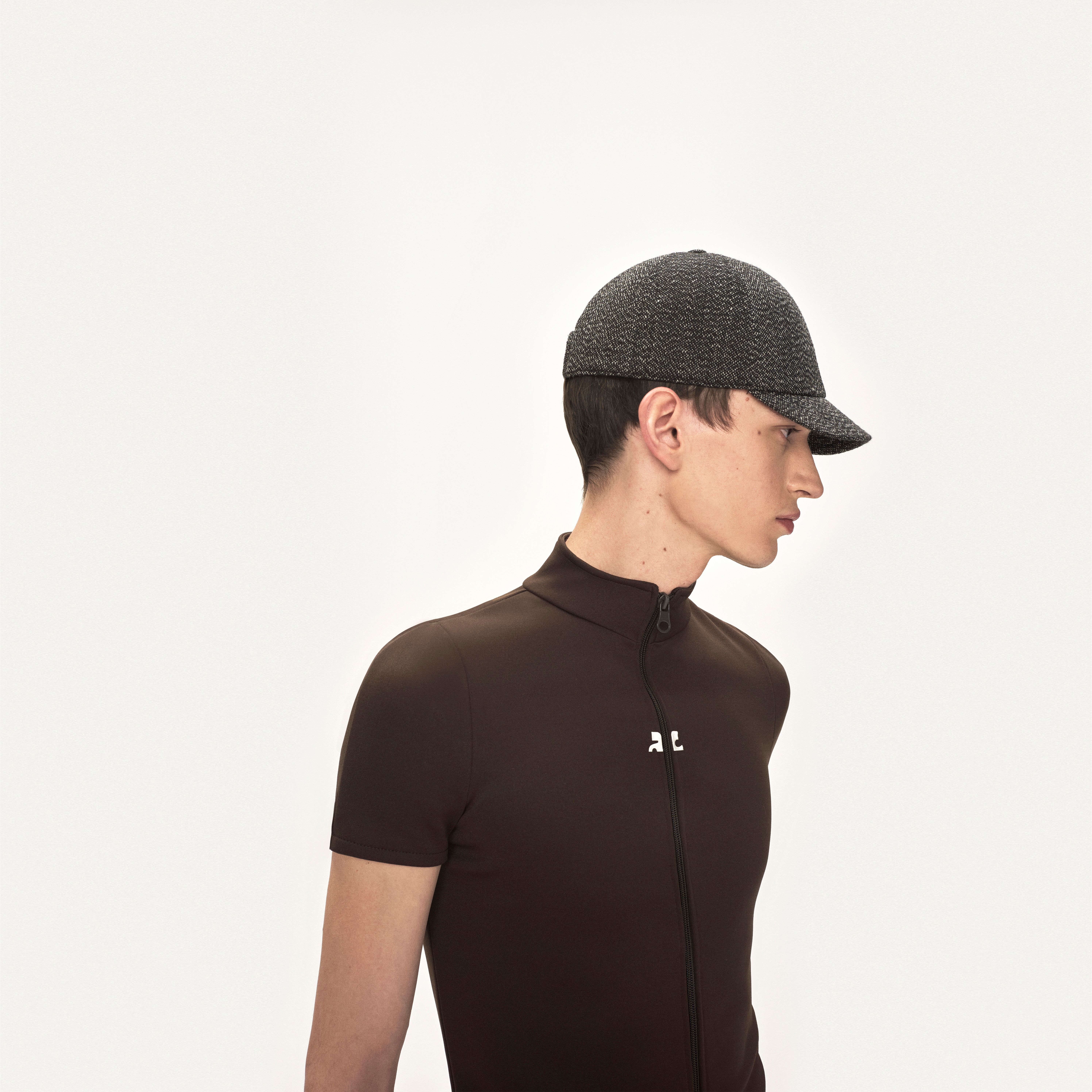 Elegant male model wearing Courrèges sporty black zip-up top with a cap, minimalist style.