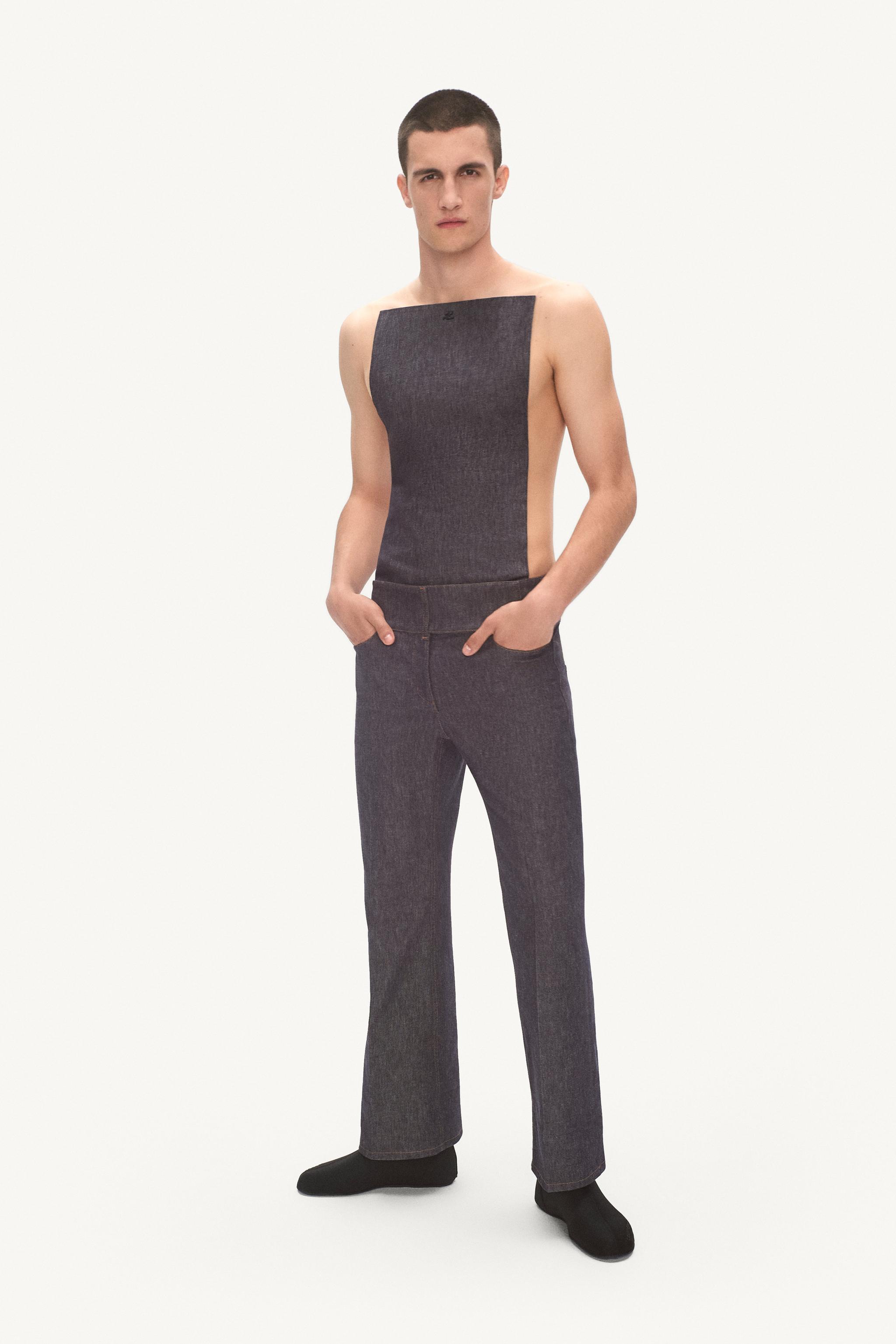 Elegant male model in dark denim outfit, showcasing Courrèges fashion in a minimal studio setting.