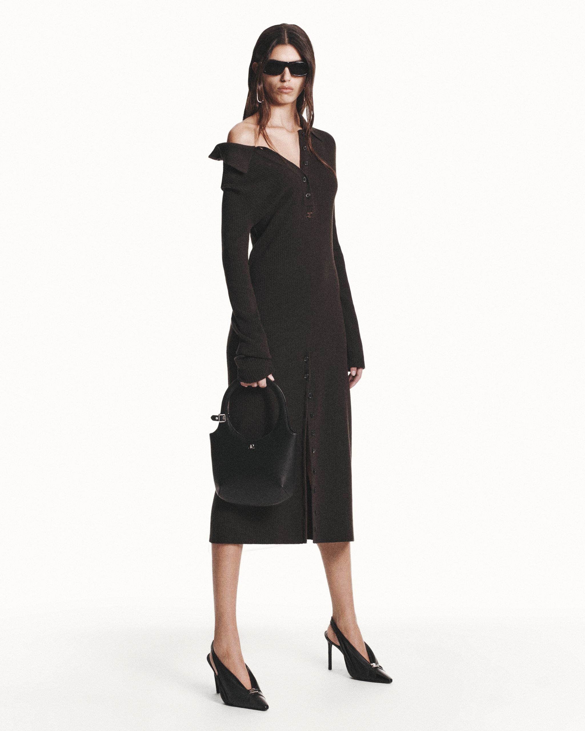 Elegant woman in black Courrèges dress, wearing sunglasses, high heels, and holding a handbag.