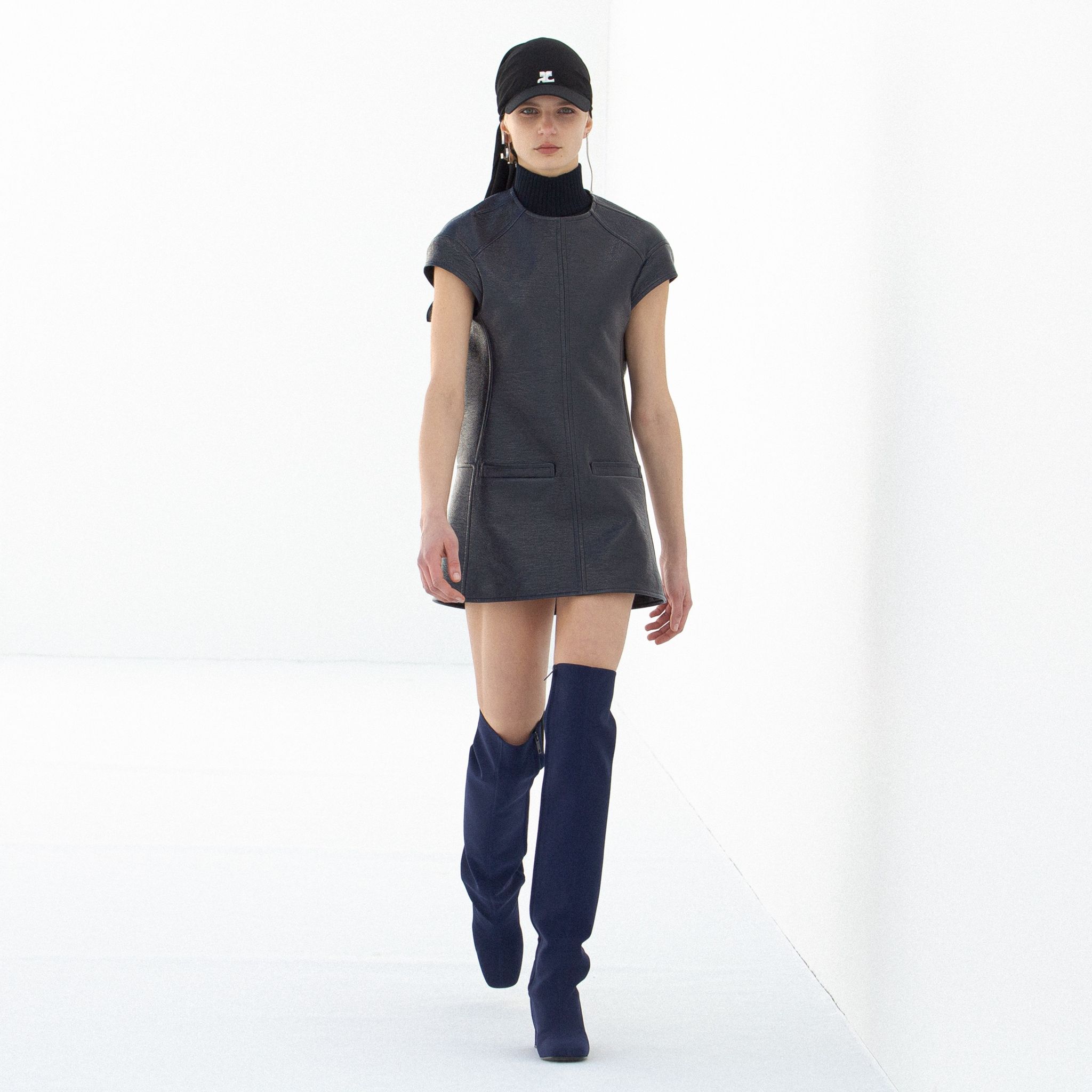 Elegant black Courrèges mini dress with high boots, showcased on a runway model.
