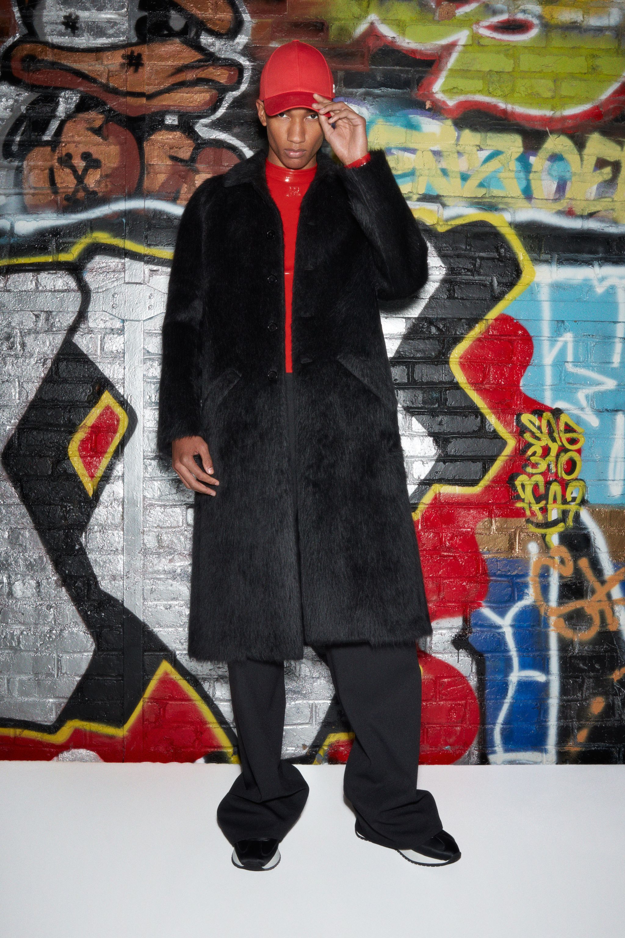 Elegant model wearing a black coat and red cap against colorful graffiti for Courrèges.