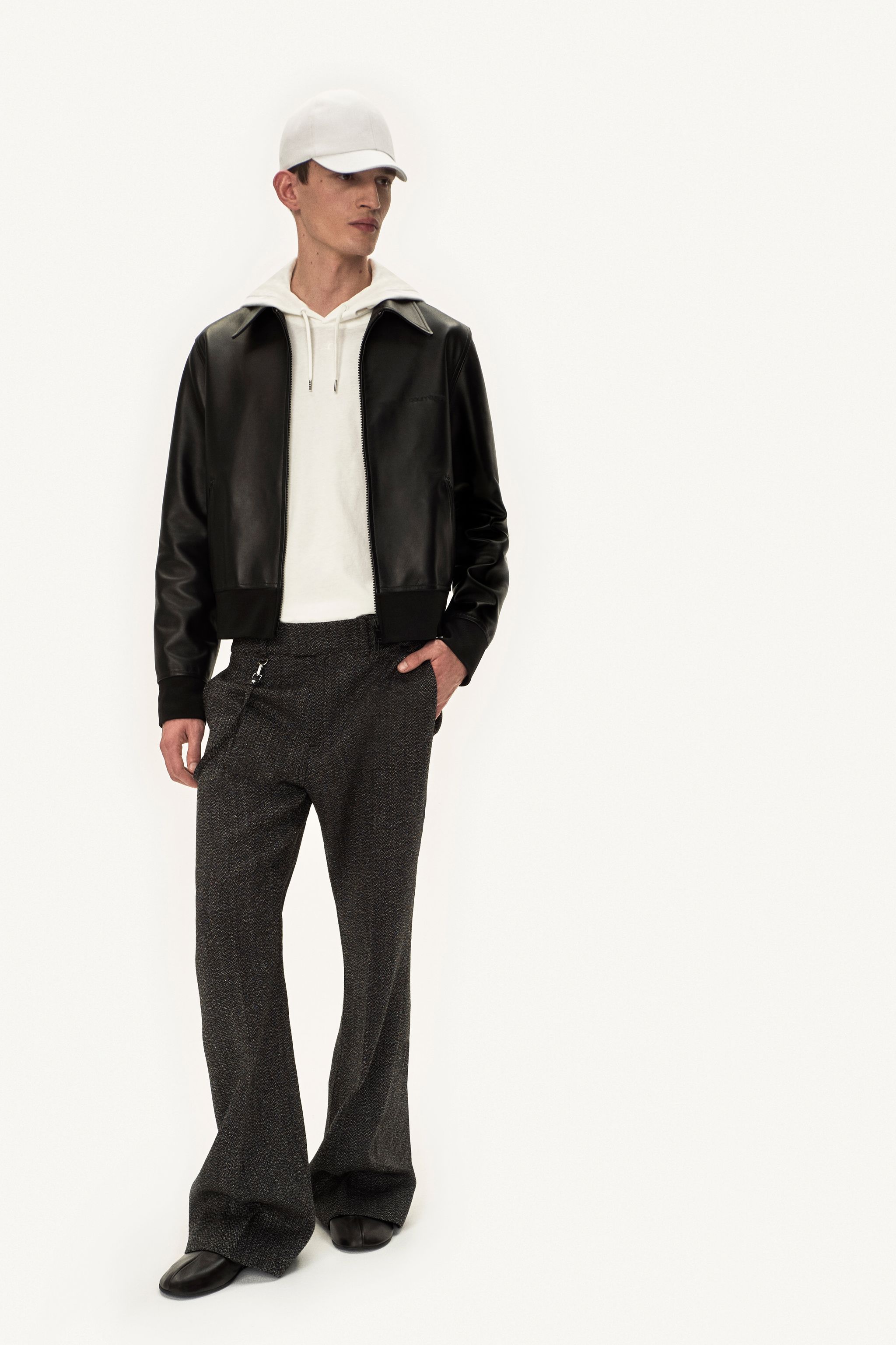 Elegant men's fashion look featuring a leather jacket, hoodie, and tailored trousers for Courrèges.