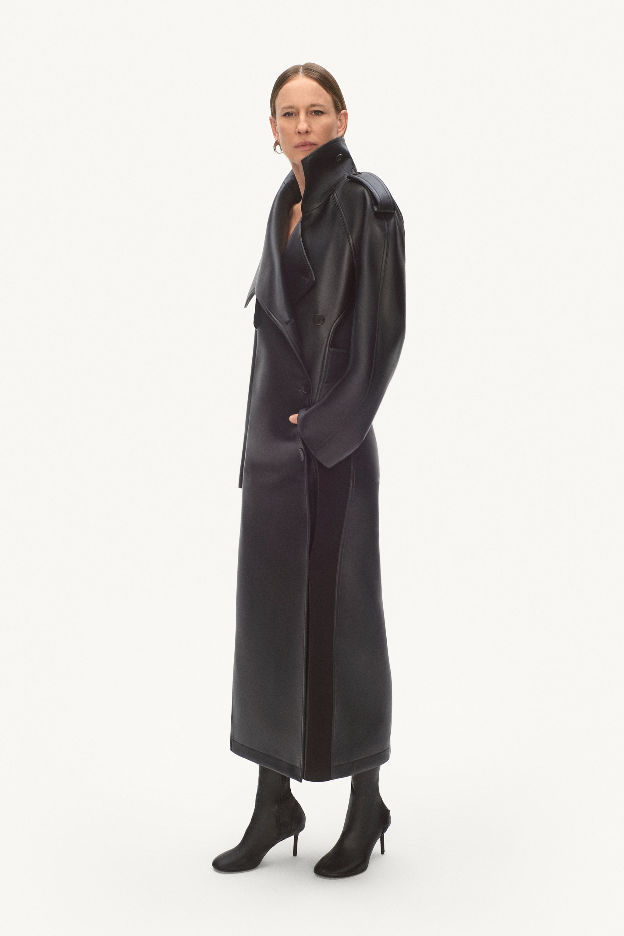 Elegant woman in a black leather trench coat and high-heeled boots, showcasing Courrèges fashion.