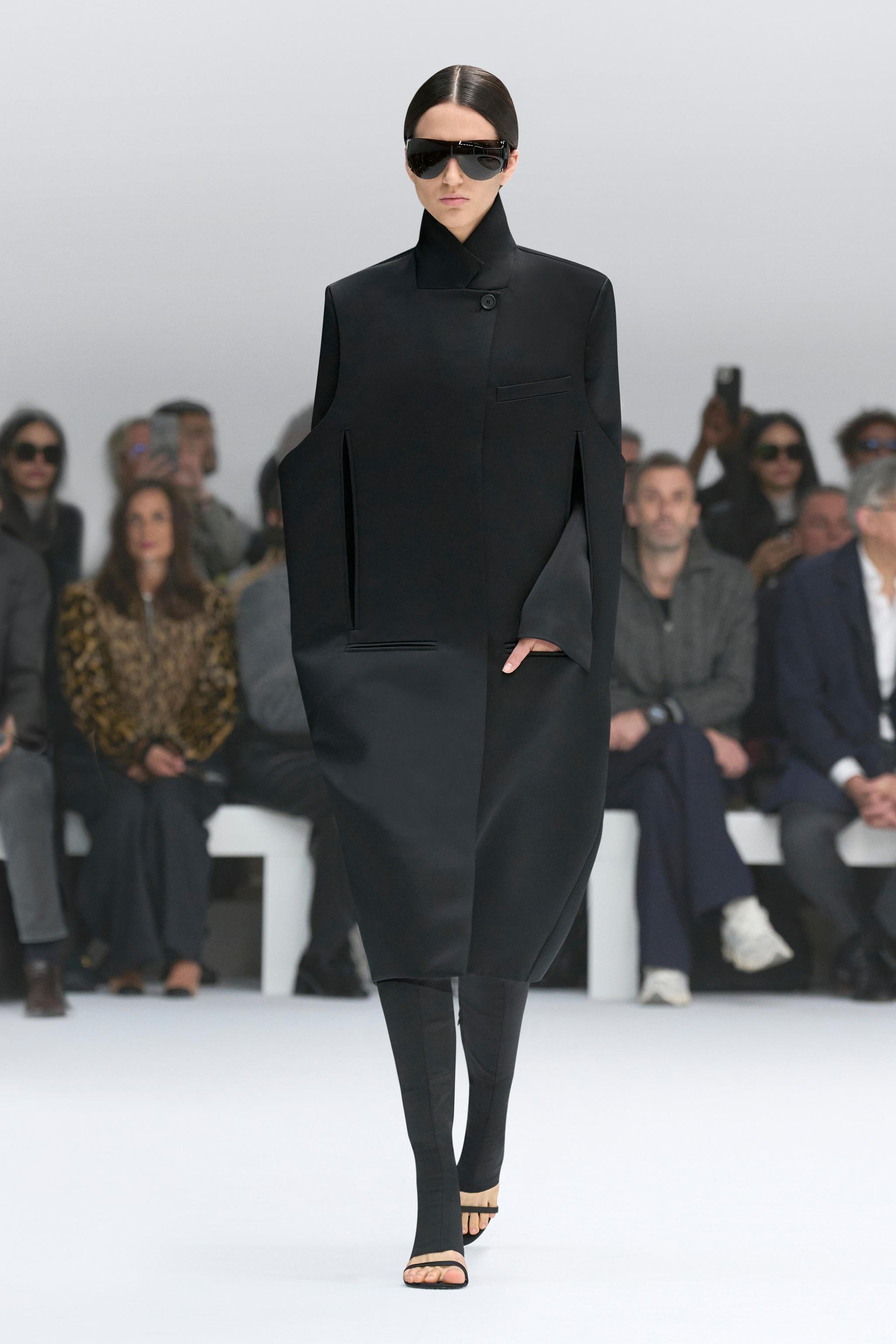 Chic black oversized coat with futuristic sunglasses, showcased on a runway for Courrèges.