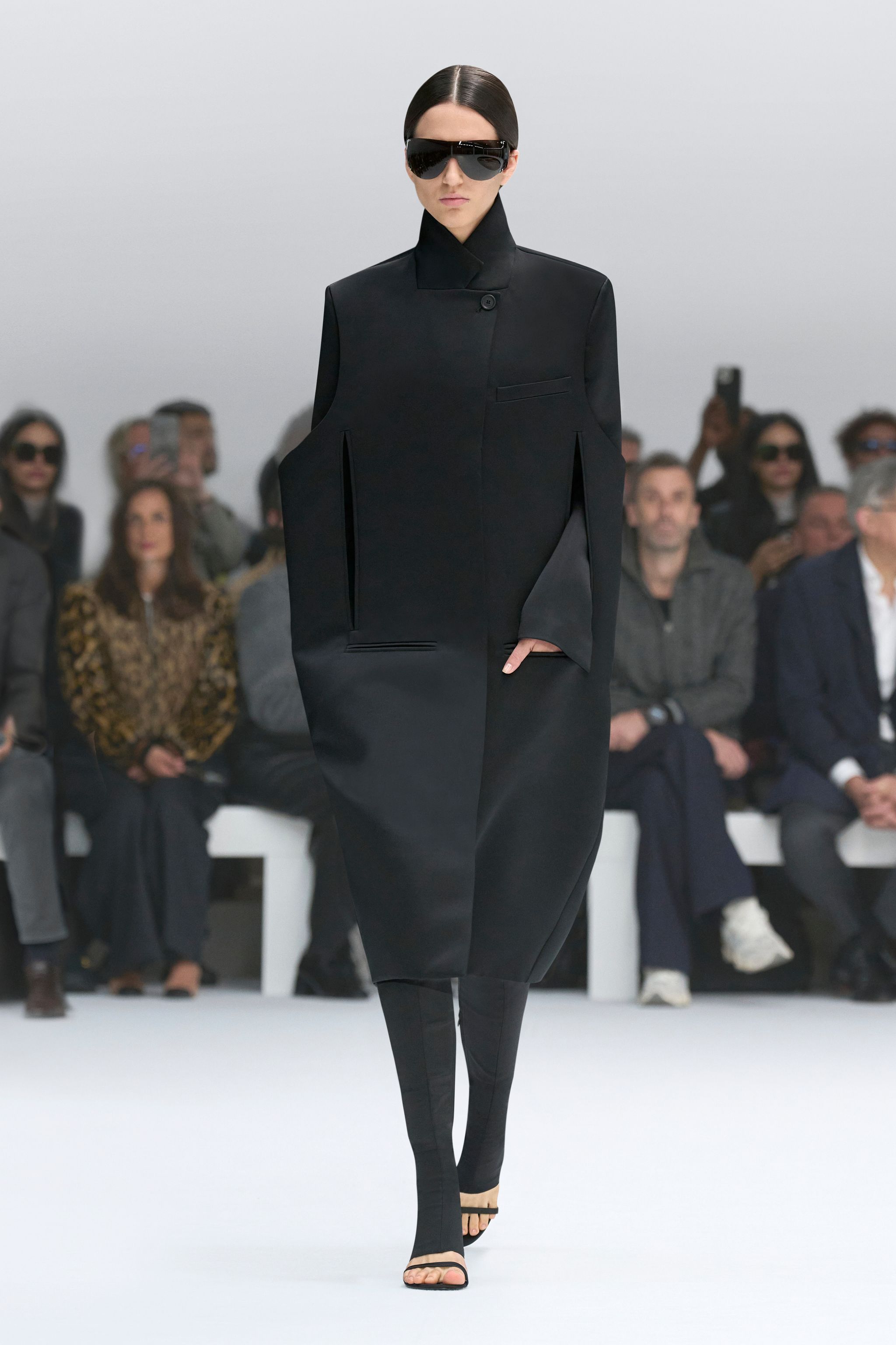 Elegant black oversized coat and sunglasses showcased on a fashion runway for Courrèges.