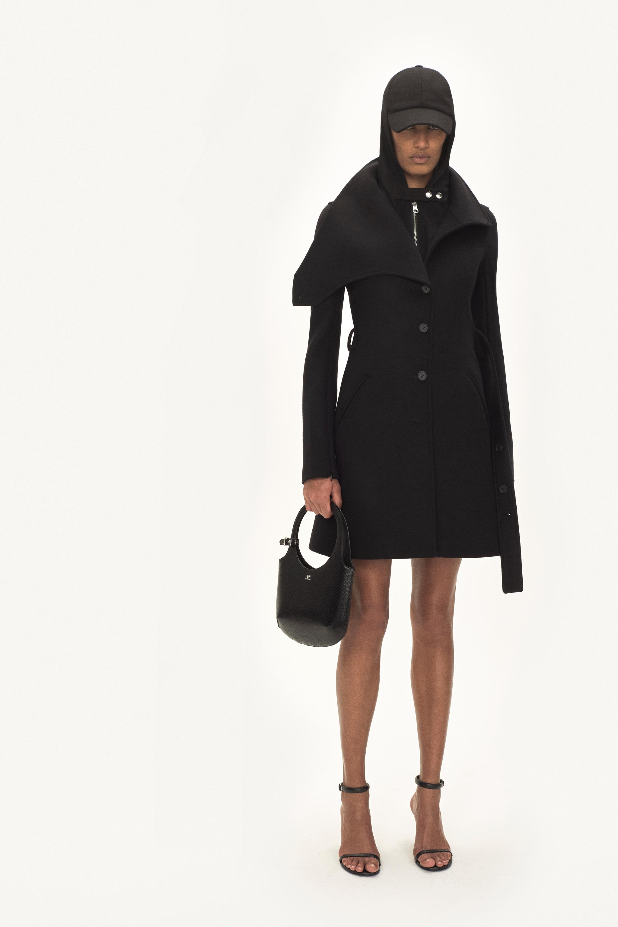 Manteau noir élégant avec capuche, associé à une casquette noire et des sandales stylées pour Courrèges.