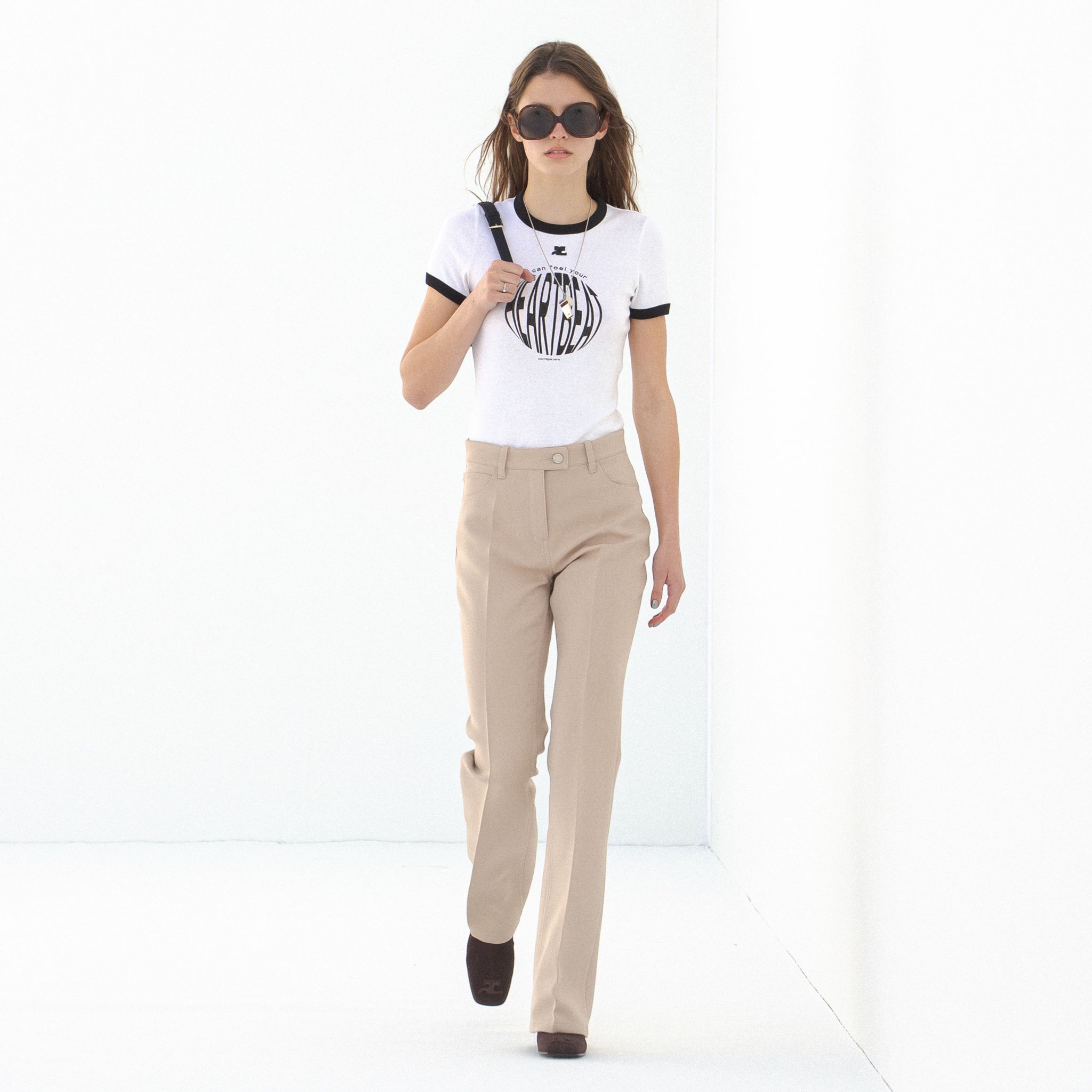 Elegant model in beige trousers and a white Courrèges t-shirt, showcasing modern fashion.