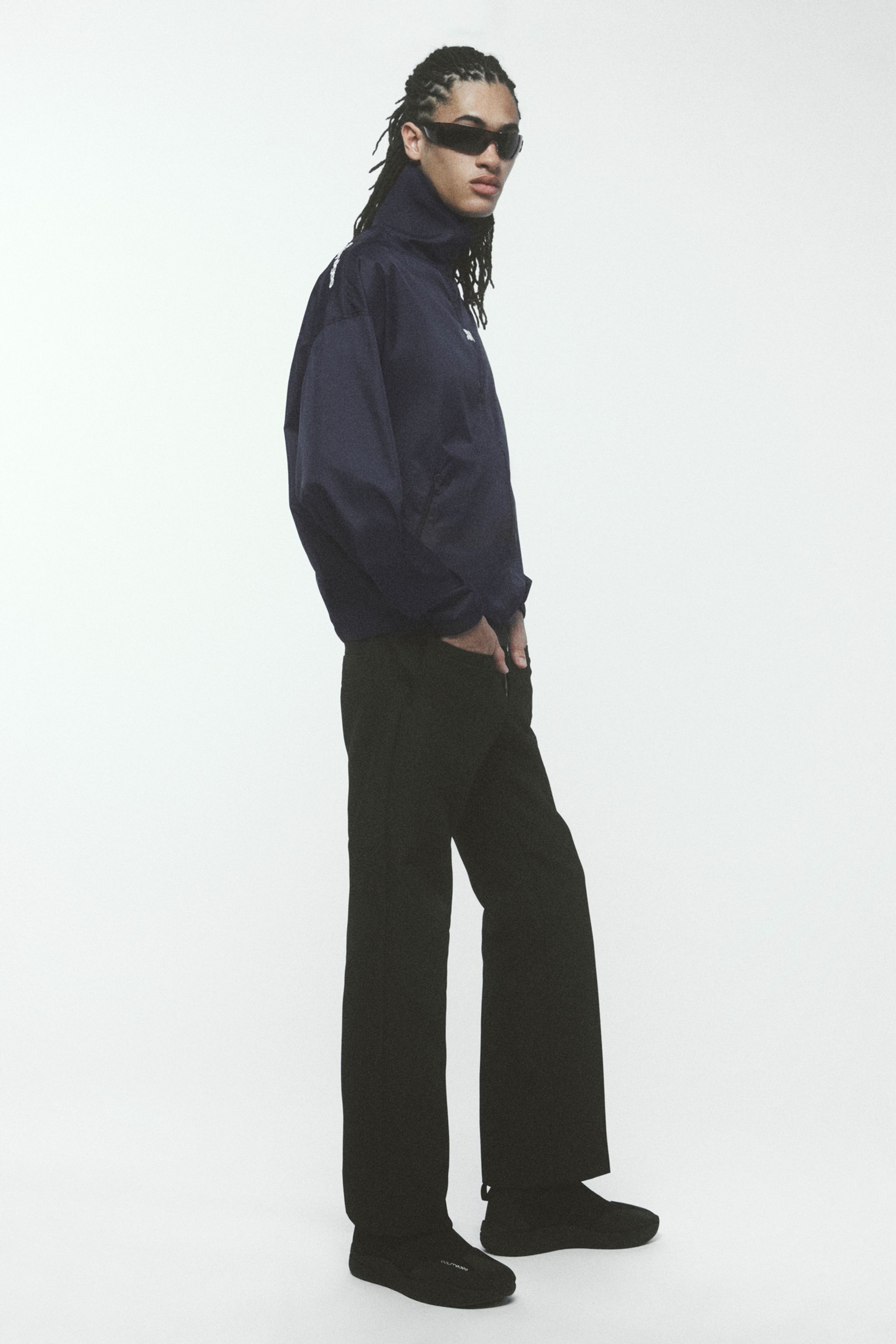 Elegant Courrèges fashion featuring a woman in a navy jacket, black pants, and sunglasses.