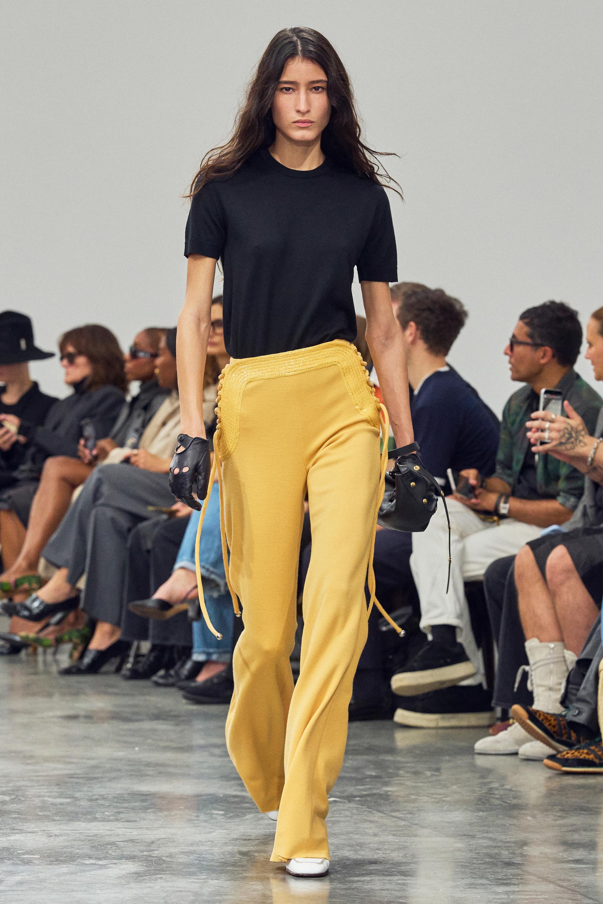 Elegant fashion runway model wearing Courrèges black T-shirt and yellow wide-leg pants.