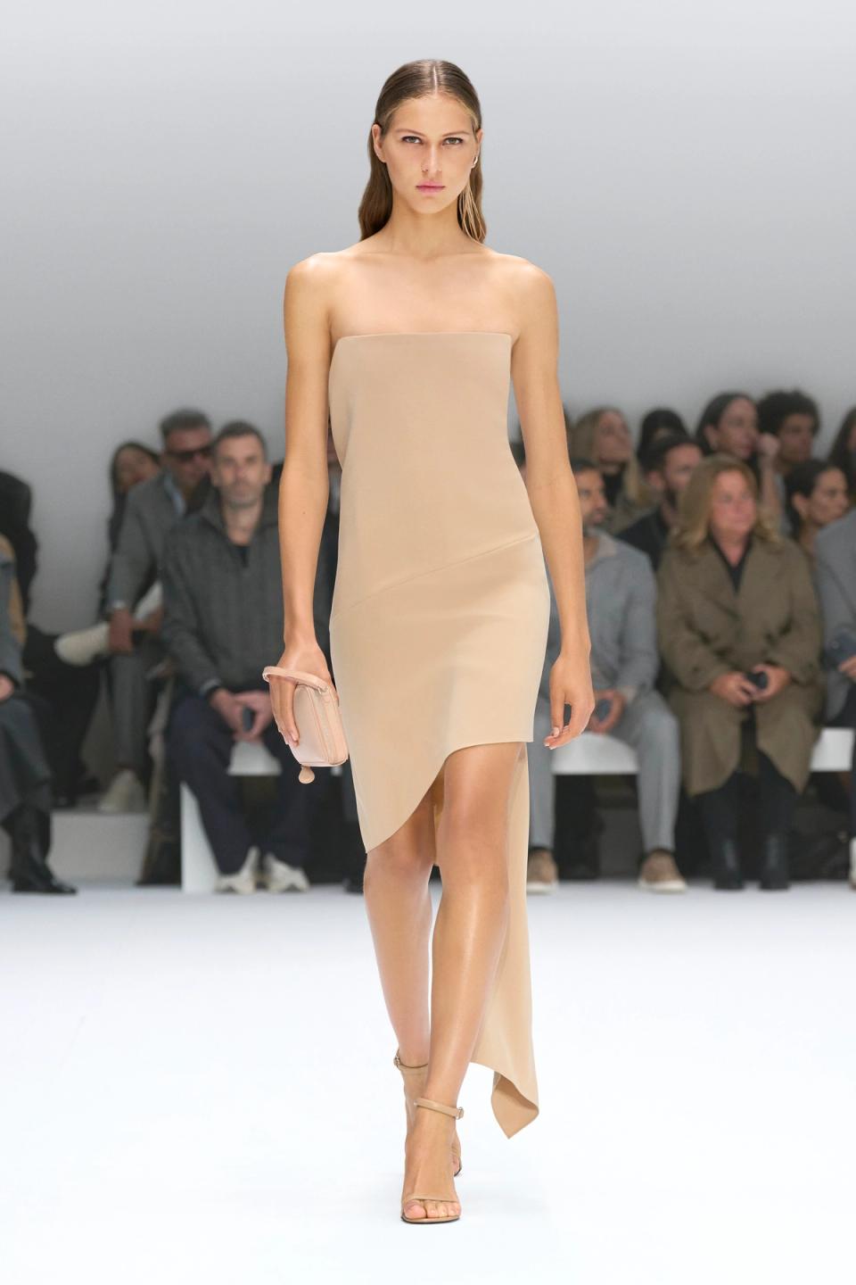 Elegant model wearing a beige strapless dress on Courrèges fashion runway, showcasing chic style.