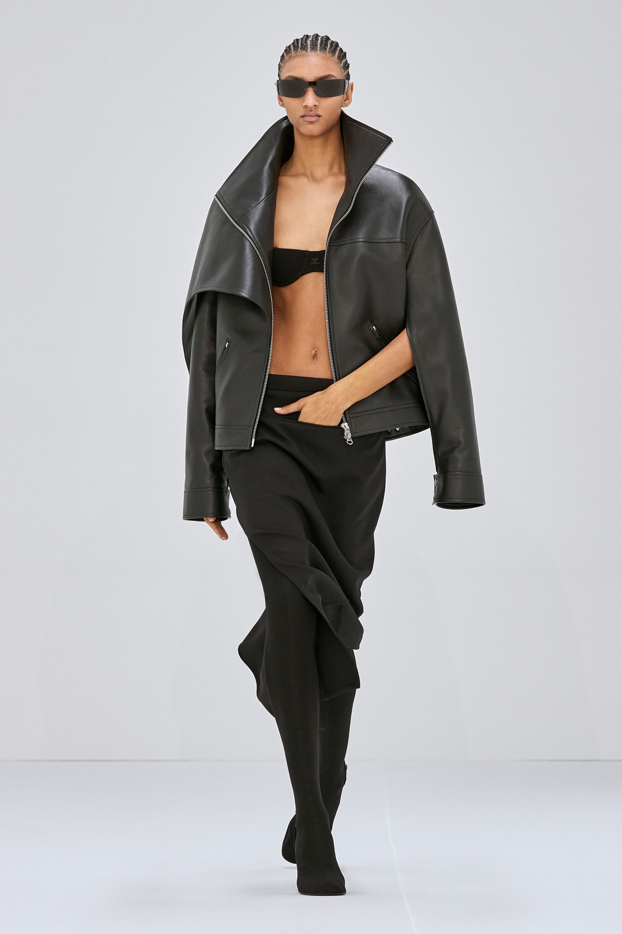 Elegant model in black leather jacket, sunglasses, and stylish black outfit for Courrèges fashion.