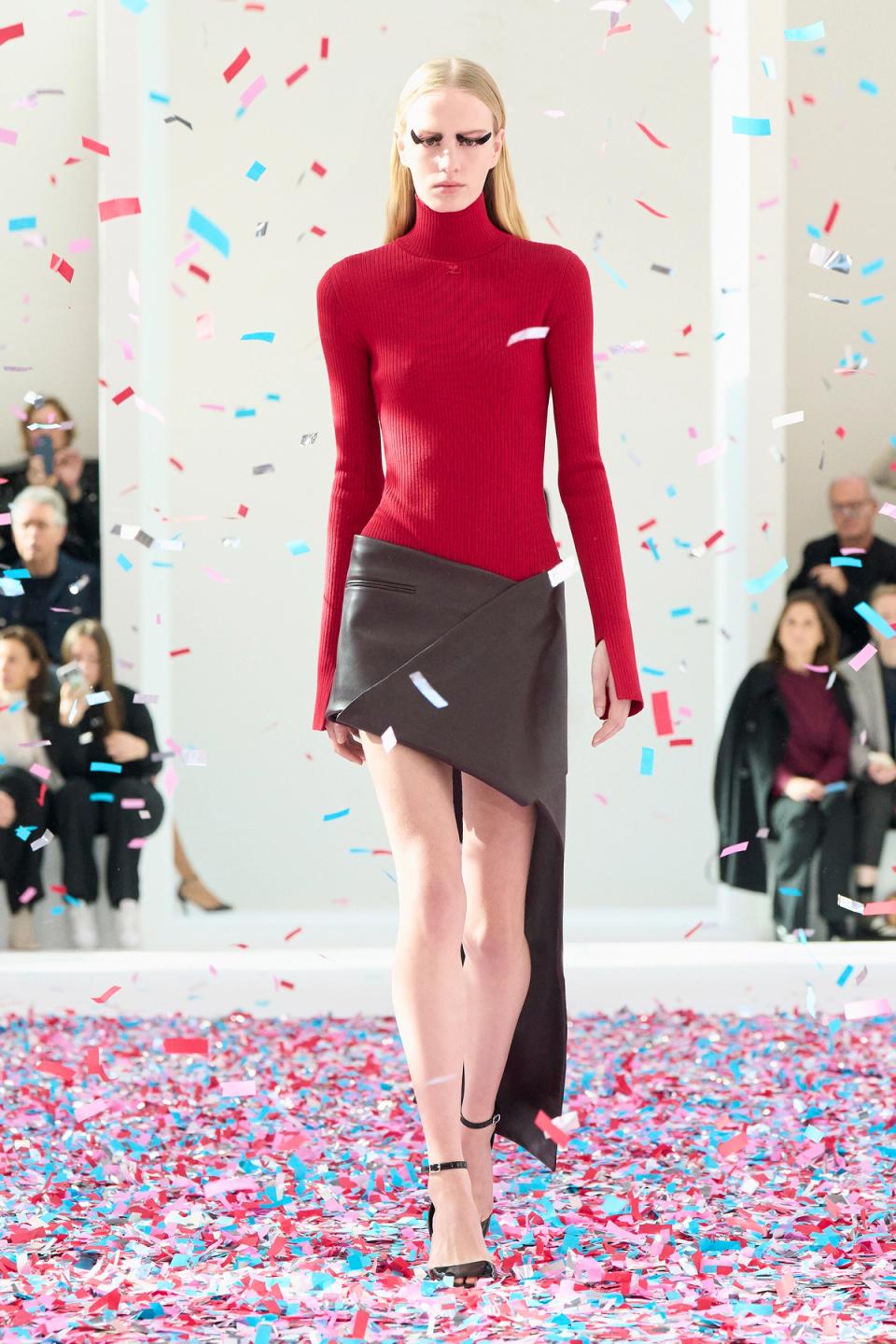 Elegant fashion runway model wearing a red turtleneck and asymmetric black skirt for Courrèges.