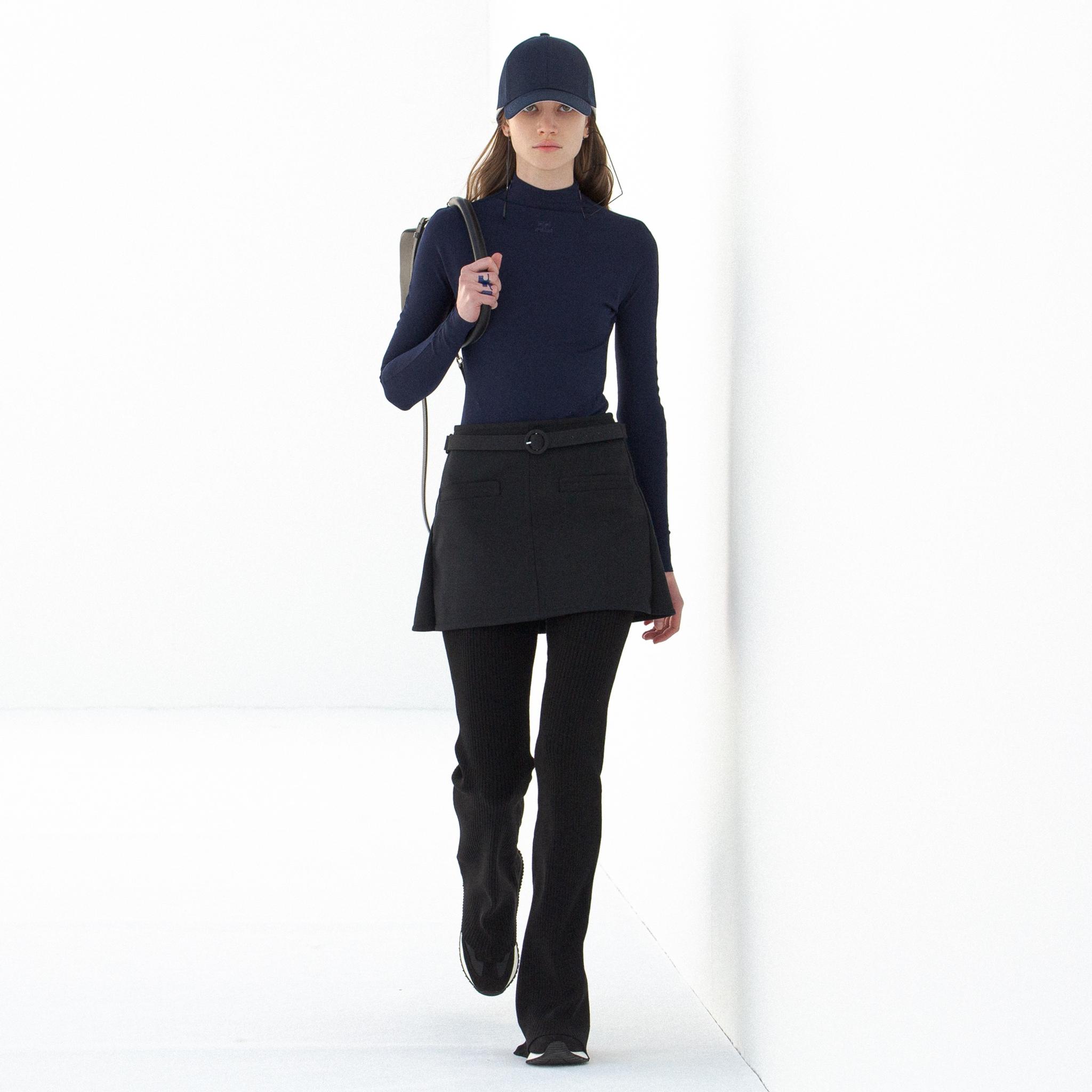 Tenue élégante bleu marine avec col roulé, jupe et casquette, pour le site e-commerce de Courrèges.