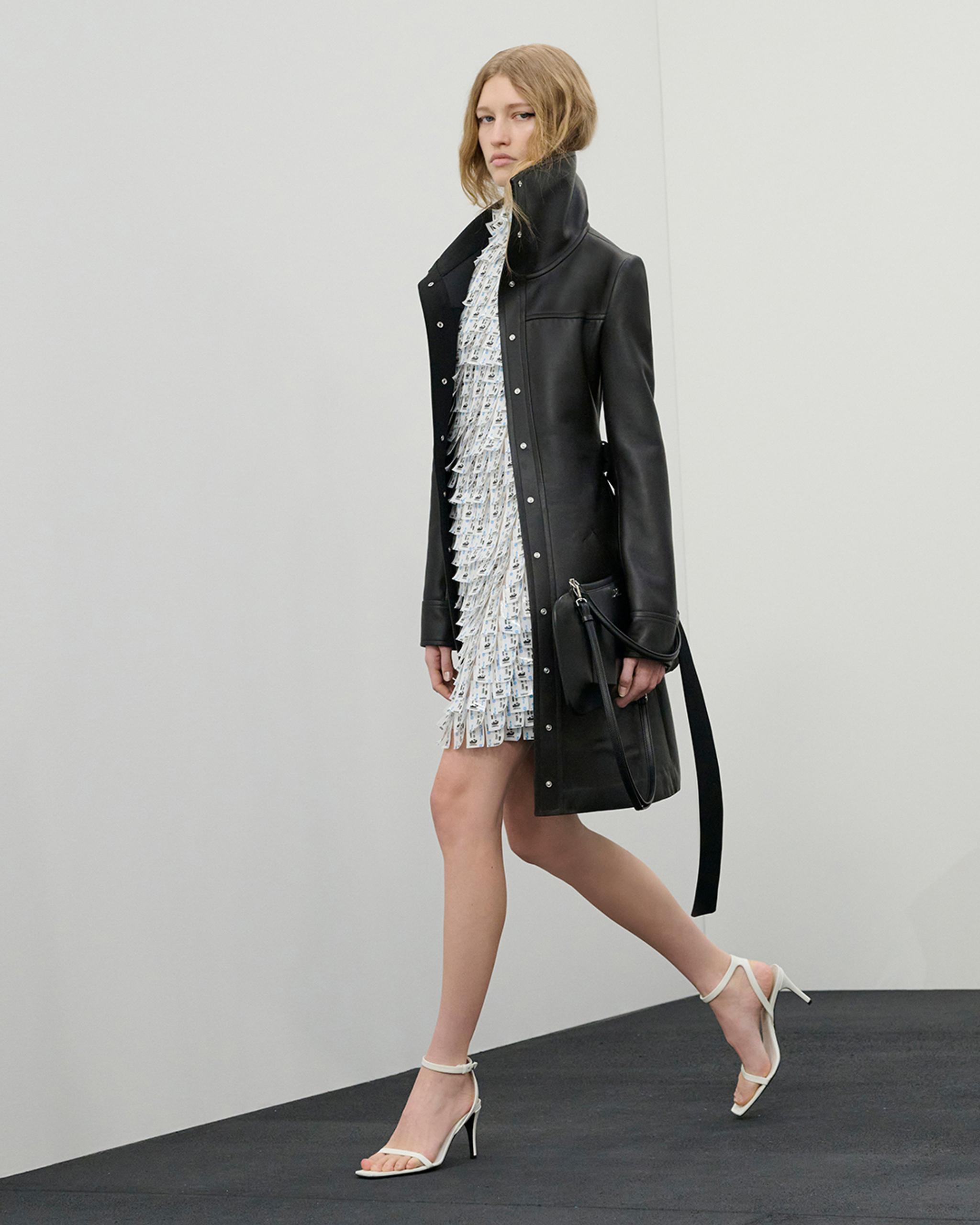 Elegant woman in a black leather coat and white dress, showcasing Courrèges fashion pieces.