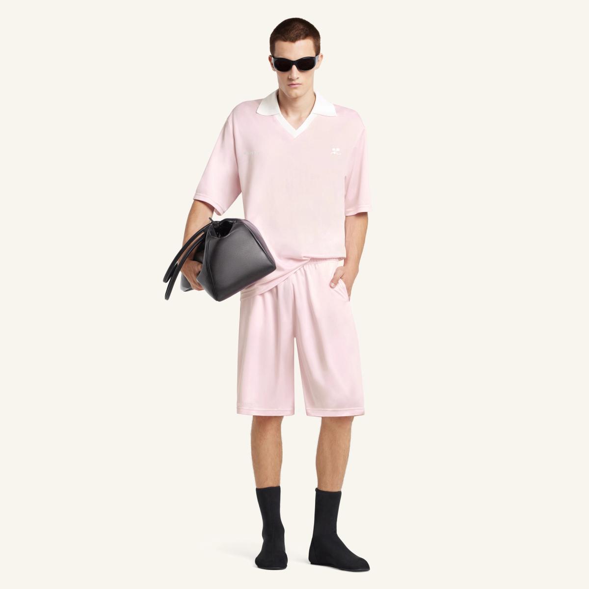 Fashion model wearing pink Courrèges casual shirt, shorts, sunglasses, and carrying a black bag.