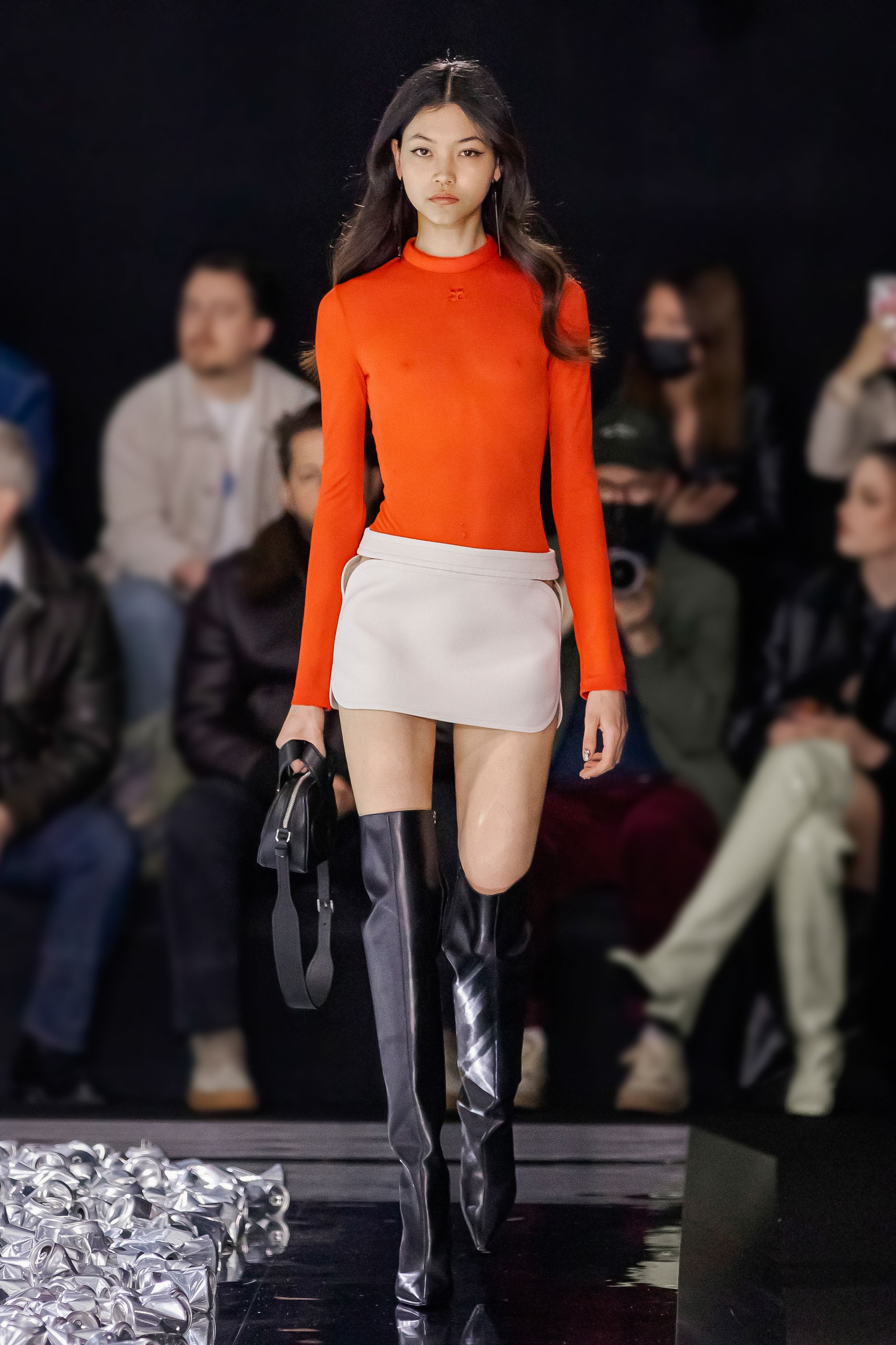 Elegant fashion runway model in Courrèges apparel, orange top, white skirt, black over-the-knee boots