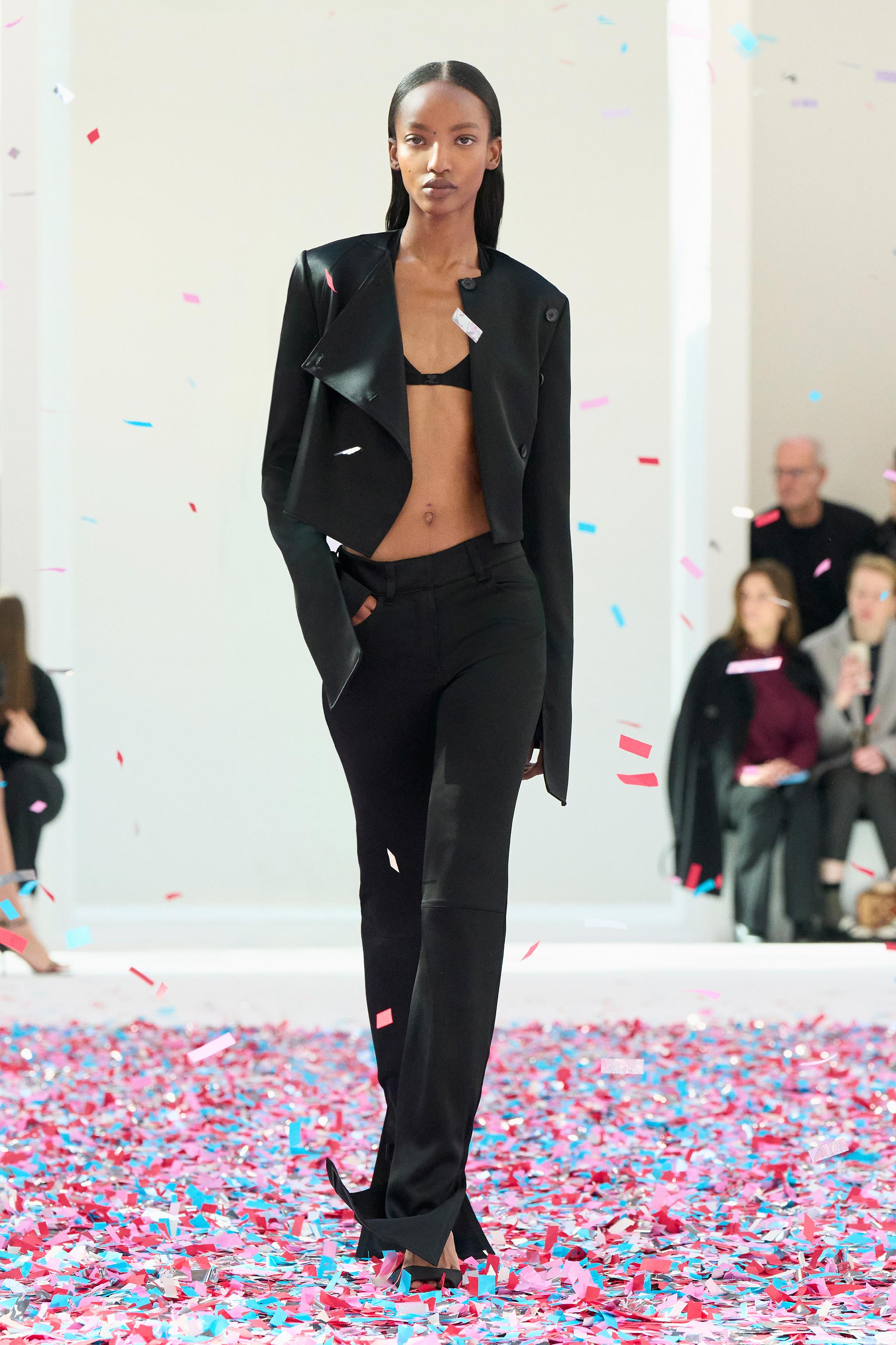 Elegant fashion runway model wearing black Courrèges ensemble, walking through confetti.