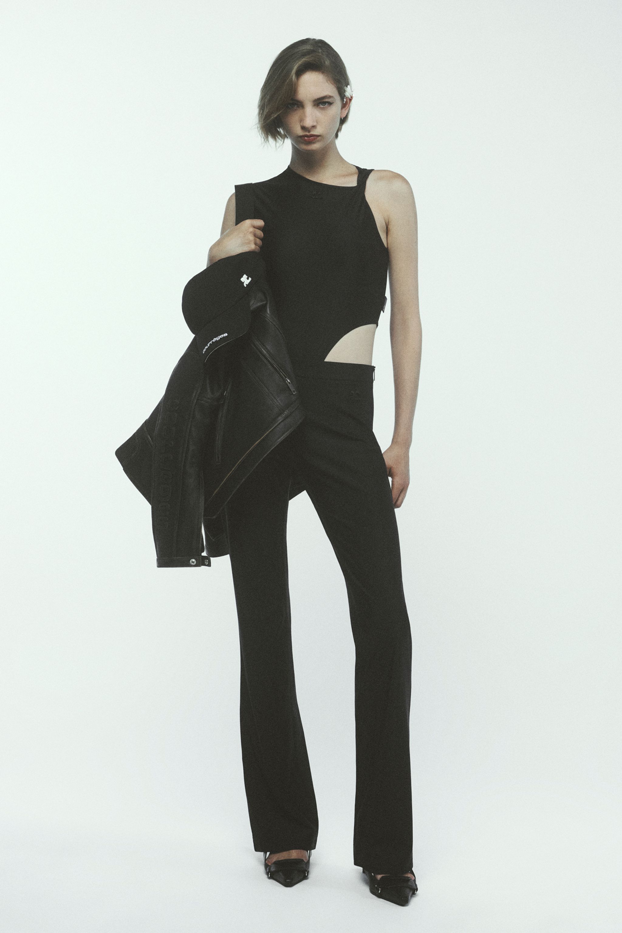 Elegant black designer outfit featuring a cut-out top, high-waisted pants, and a Courrèges bag.