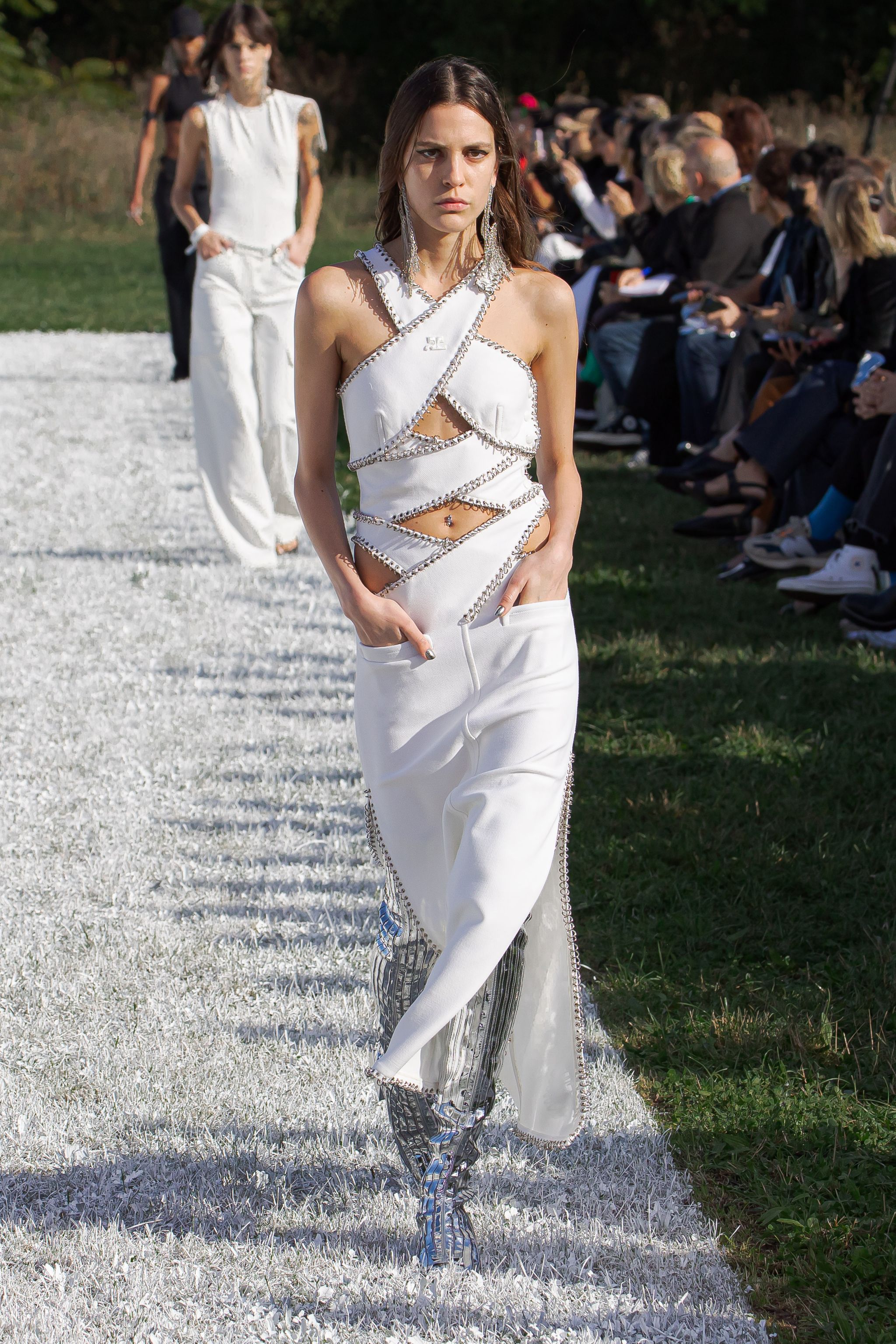 Model walking runway in white futuristic cut-out outfit for Courrèges at fashion show.