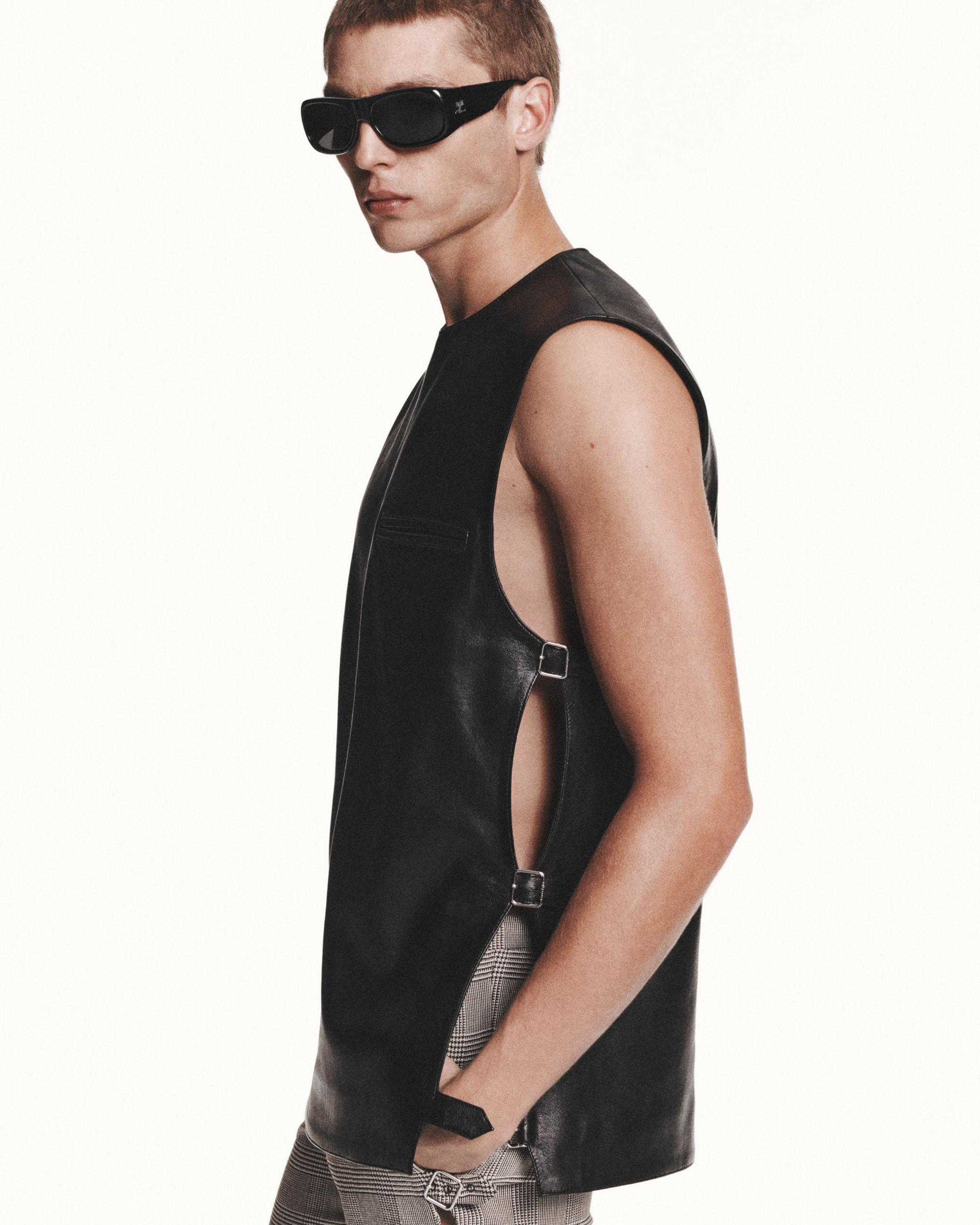 Stylish model wearing a black leather sleeveless vest and oversized sunglasses for Courrèges.