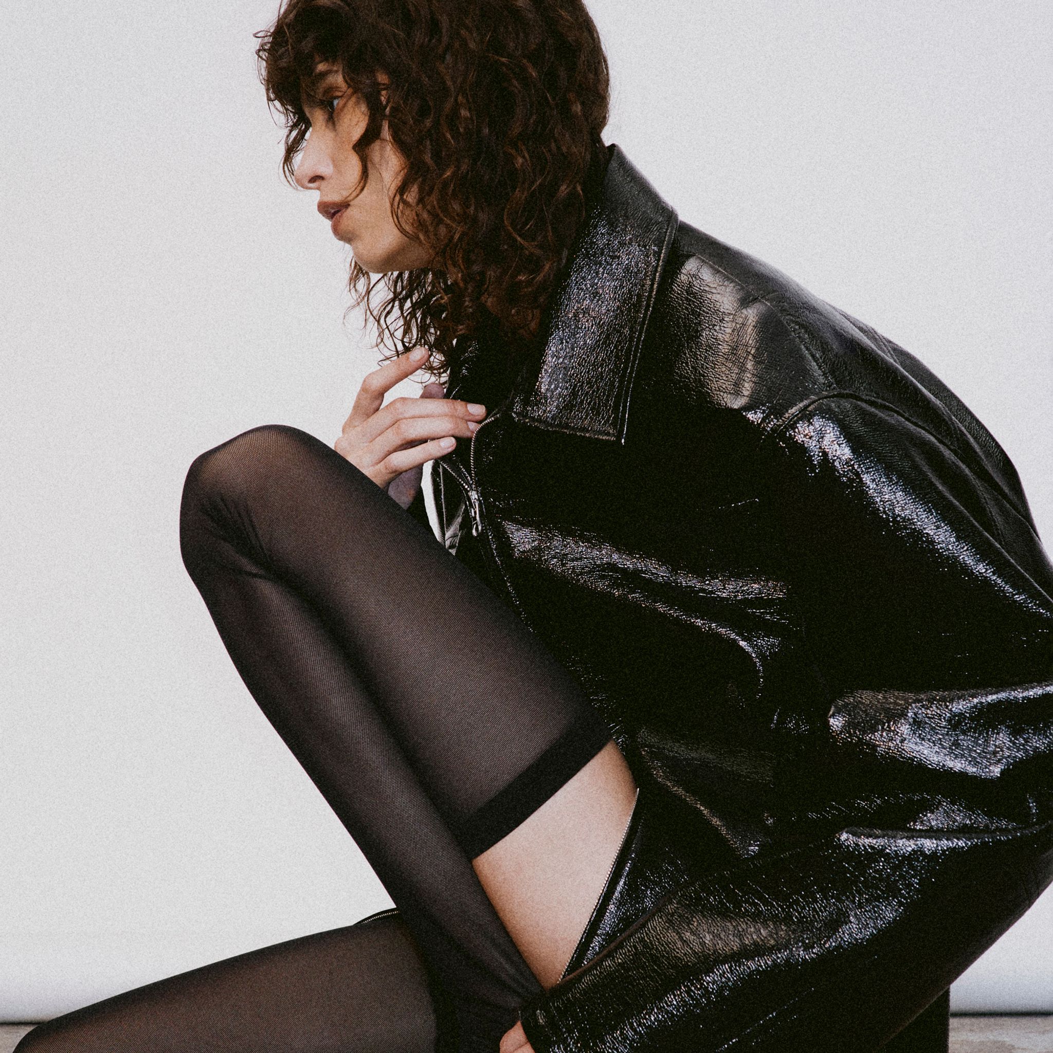 Elegant fashion model wearing black shiny leather jacket and sheer black tights for Courrèges.
