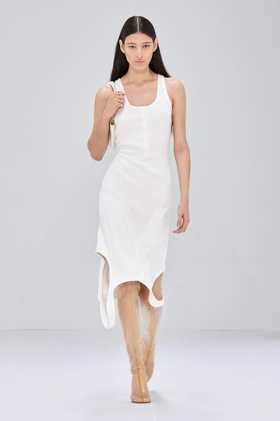 Elegant white Courrèges dress with buttons, styled with beige boots for a chic look.
