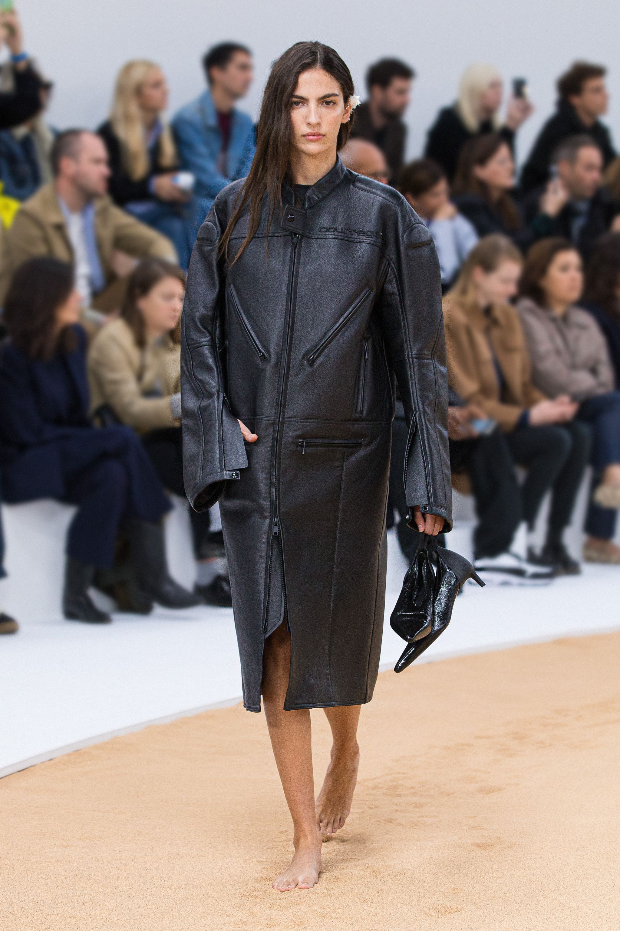 Elegant black leather coat by Courrèges showcased on a runway for an online fashion store.