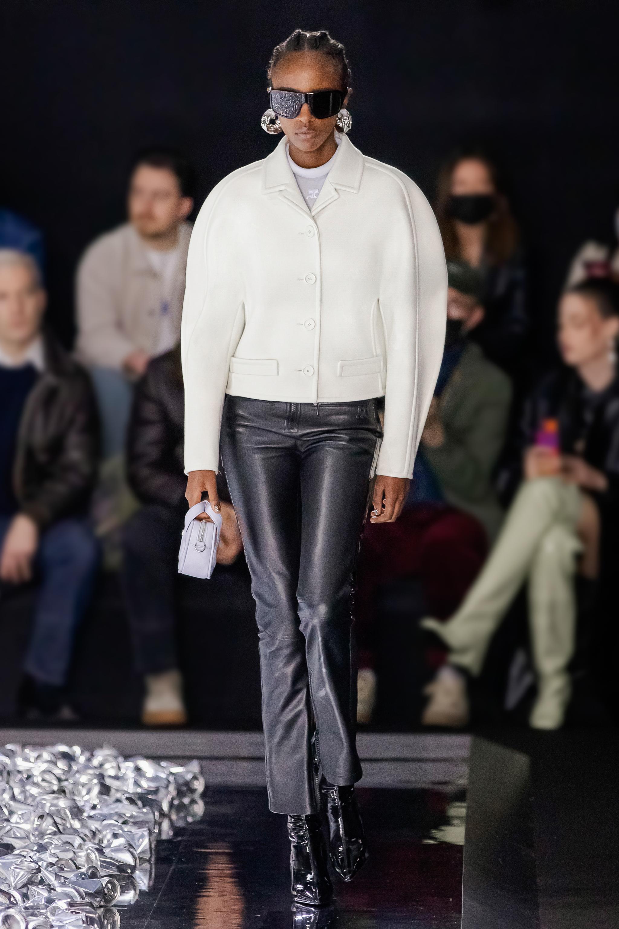 Elegant Courrèges runway look with a white jacket, black leather pants, and futuristic accessories.