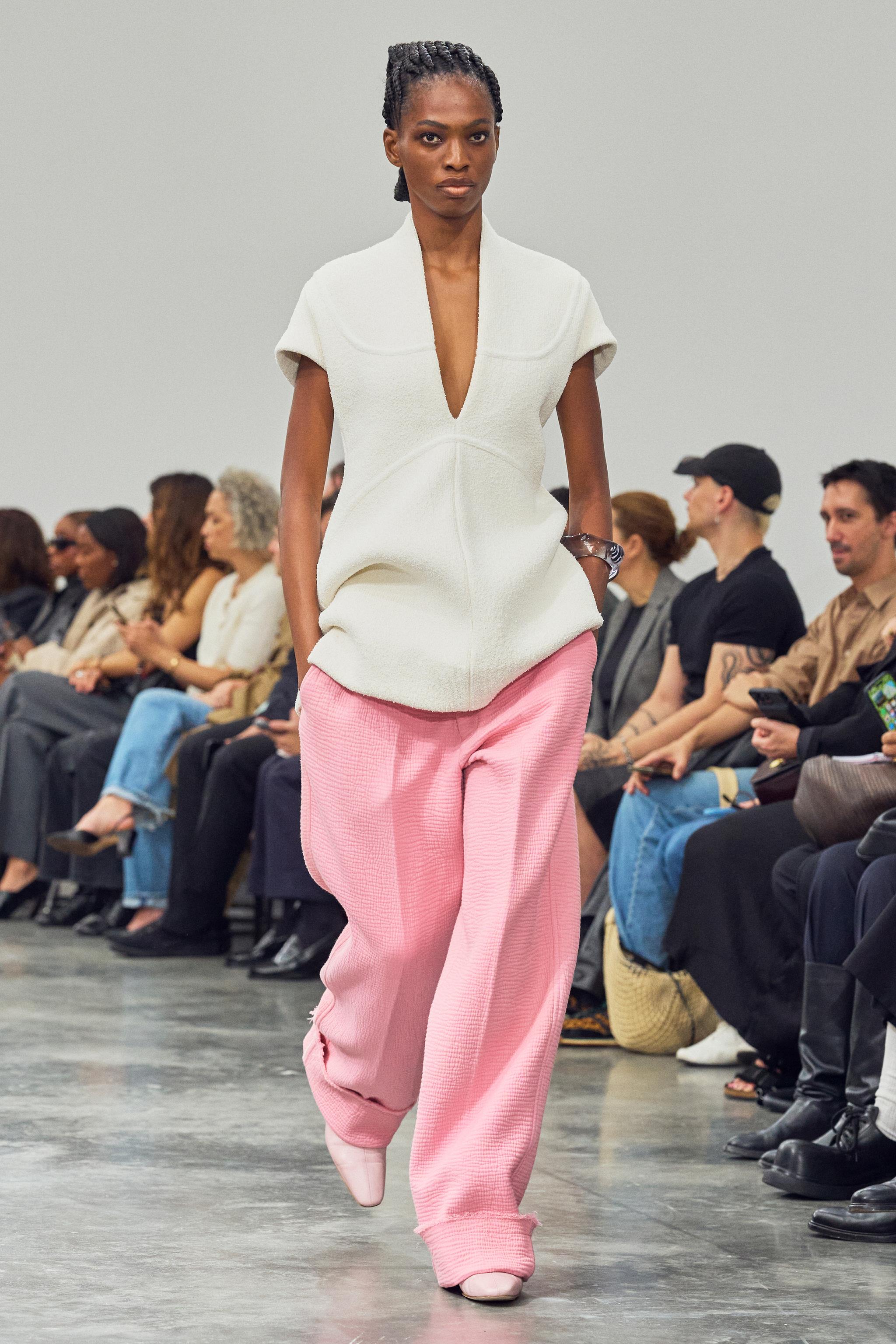 Elegant model walking runway in white top and pink wide-leg pants for Courrèges.