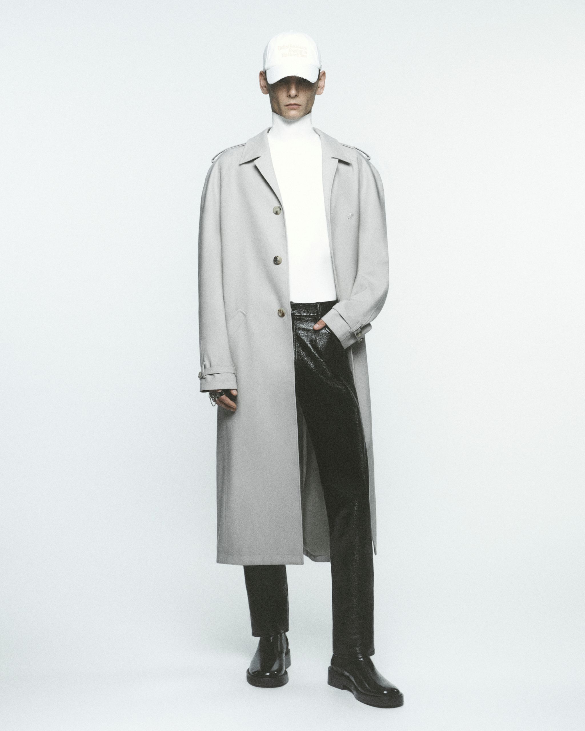 Modèle élégant en trench beige, col roulé blanc, pantalon en cuir noir et casquette pour Courrèges.