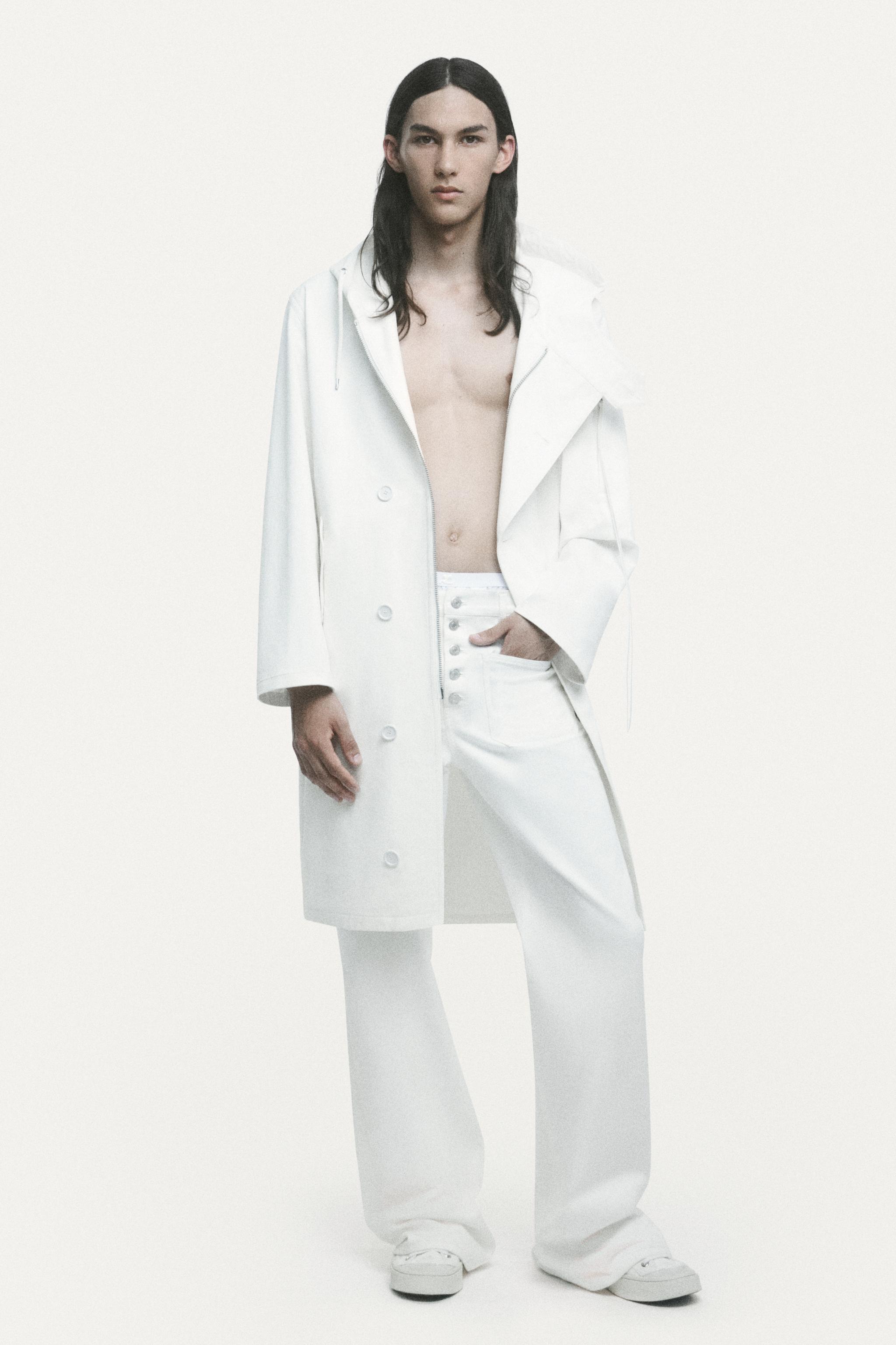 Elegant male model in white Courrèges coat and pants, showcasing modern fashion style.