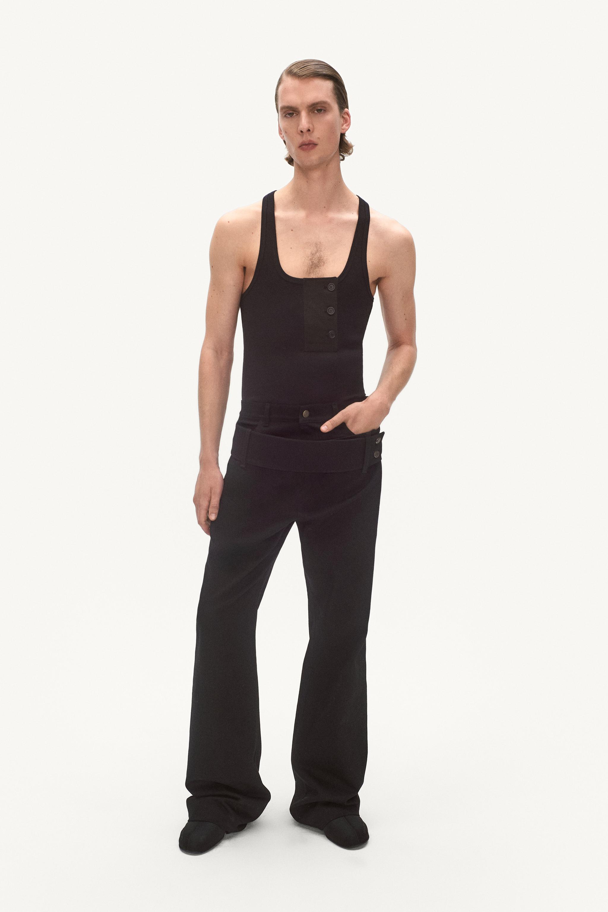 Elegant male model in black tank top and wide black pants, showcasing Courrèges fashion.
