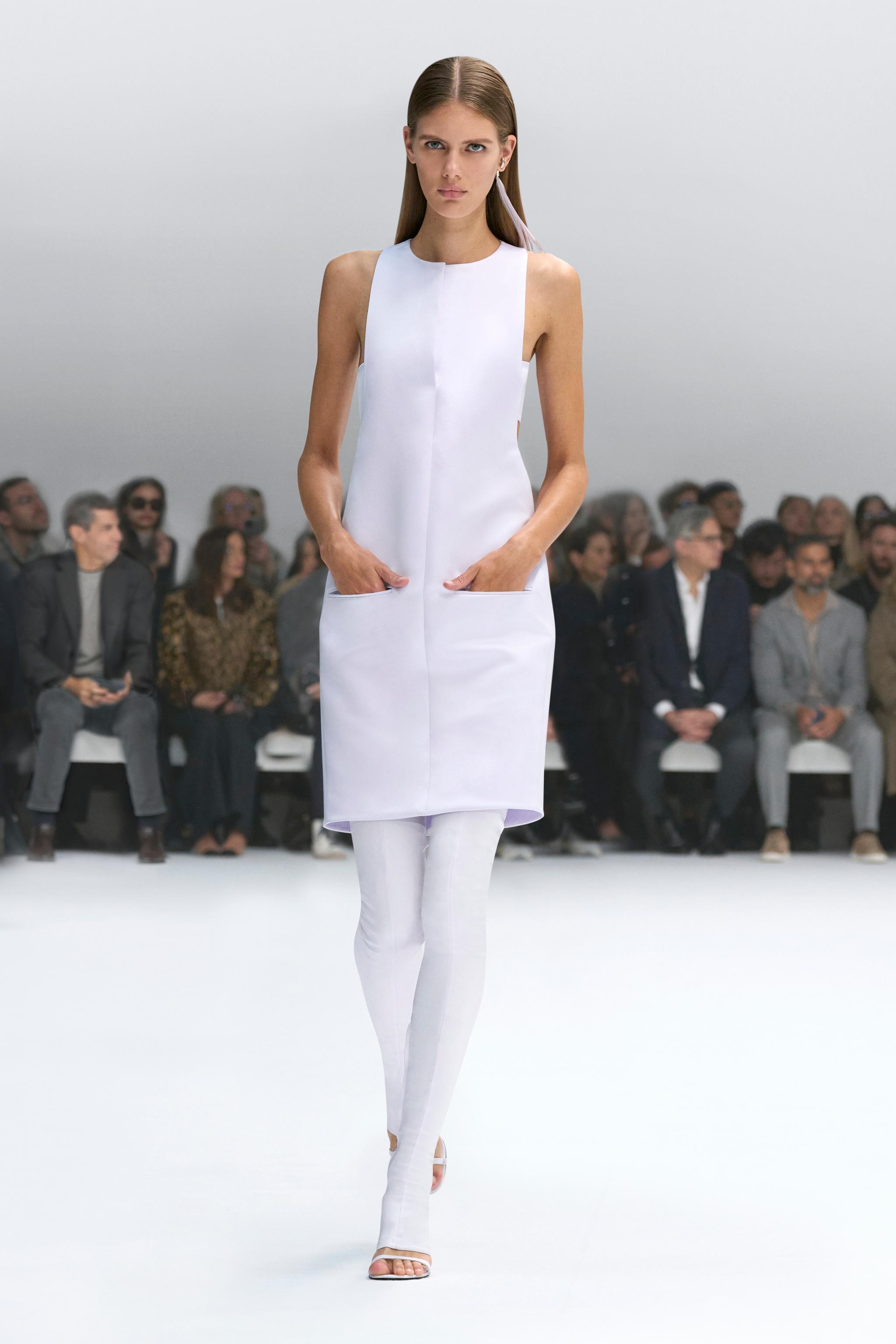 Elegant white fashion dress by Courrèges showcased on a runway at a fashion show.