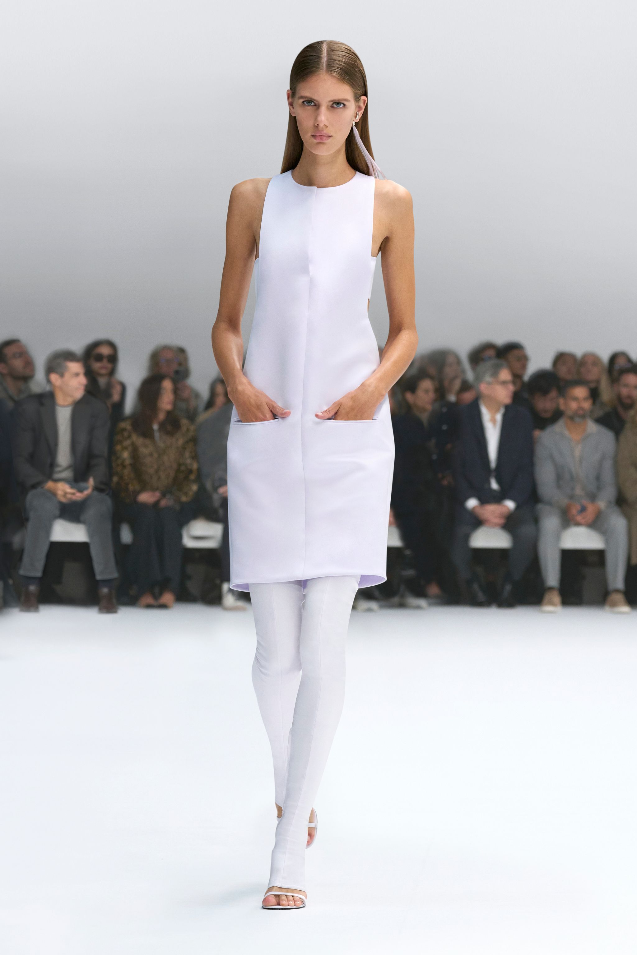 Elegant white dress with pockets showcased on a runway for Courrèges fashion brand.