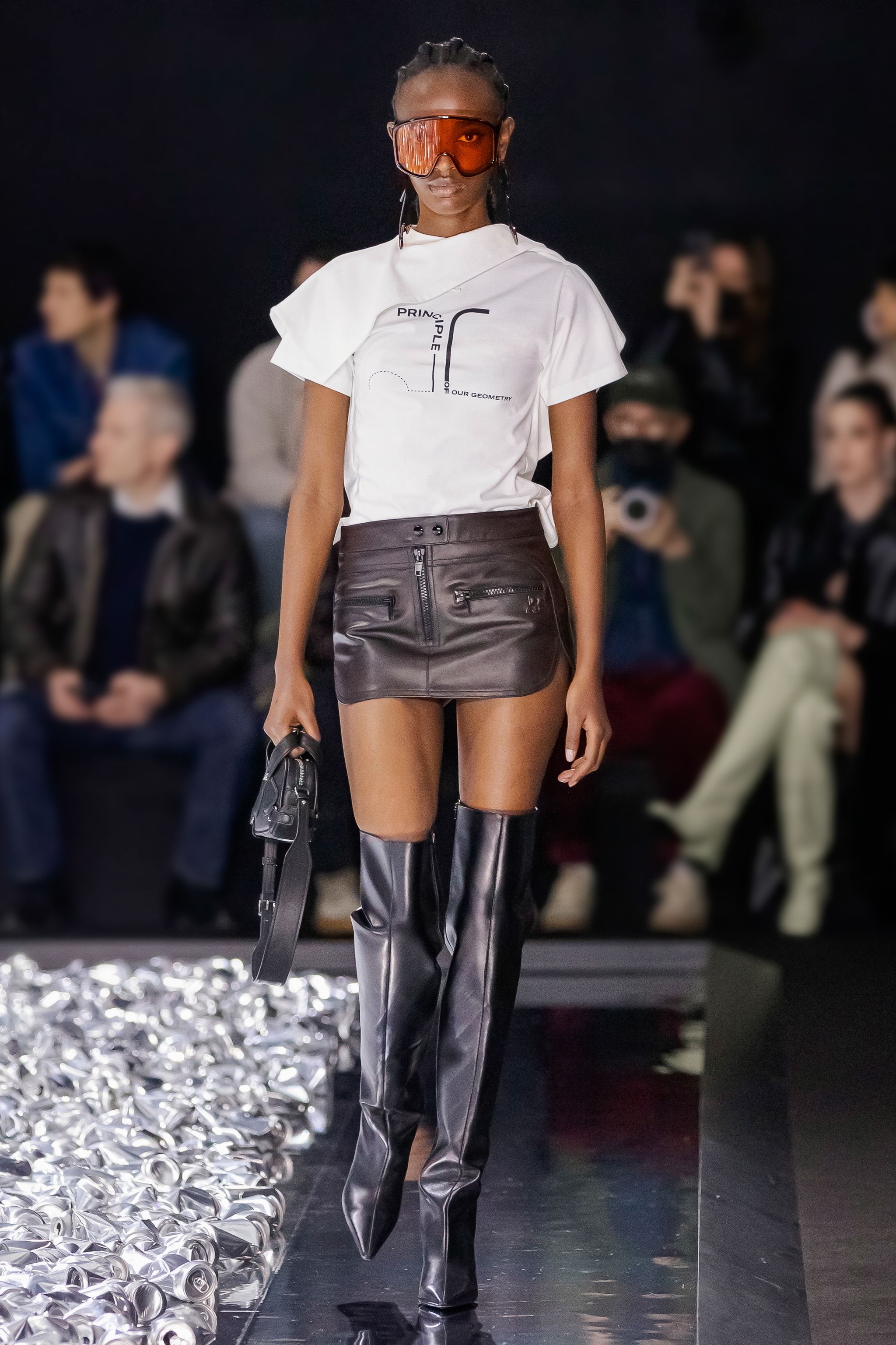 Fashion-forward model in Courrèges apparel walking runway with leather miniskirt and futuristic accessories.