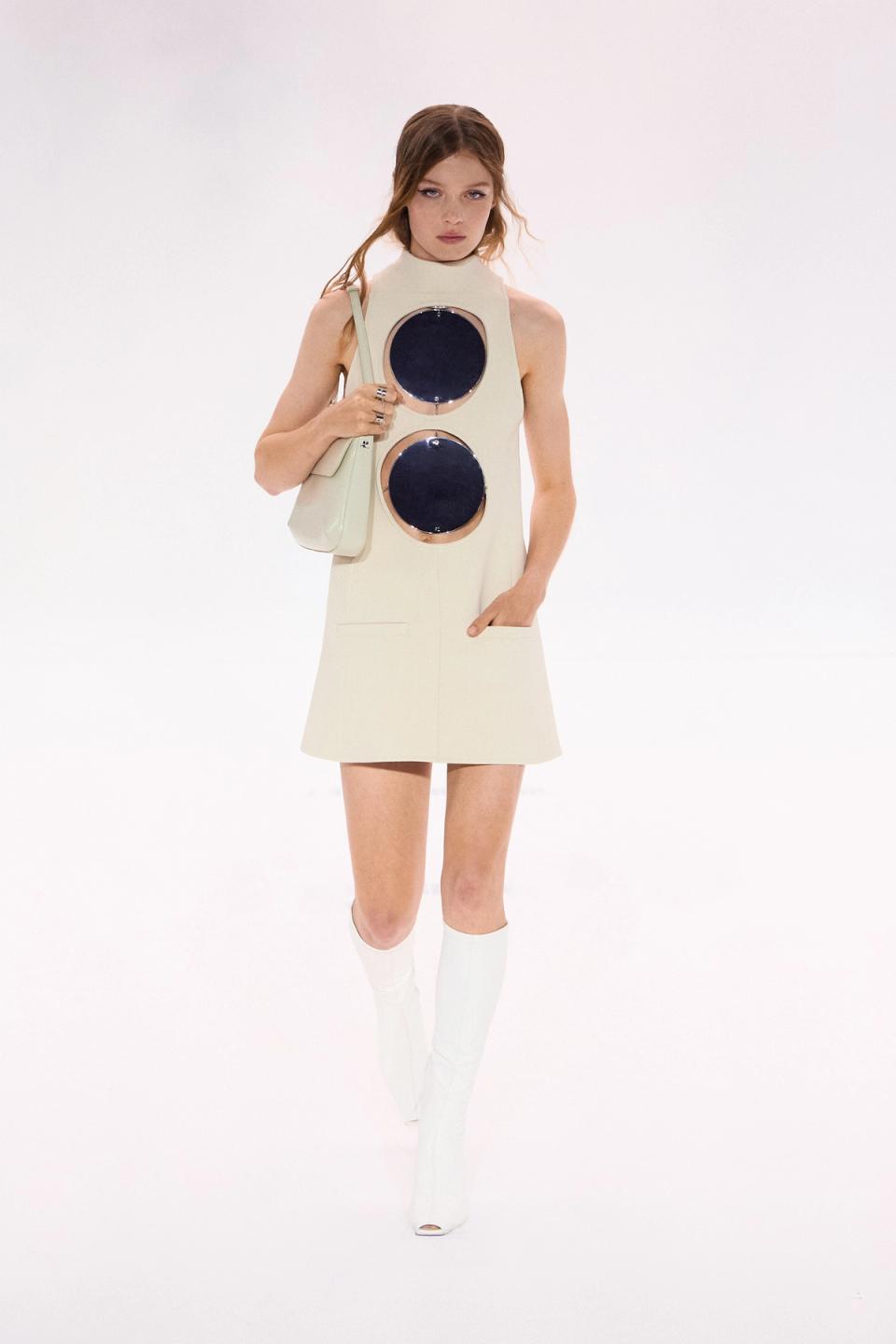 Model in a beige dress with circular mirror details, showcasing Courrèges fashion on the runway.
