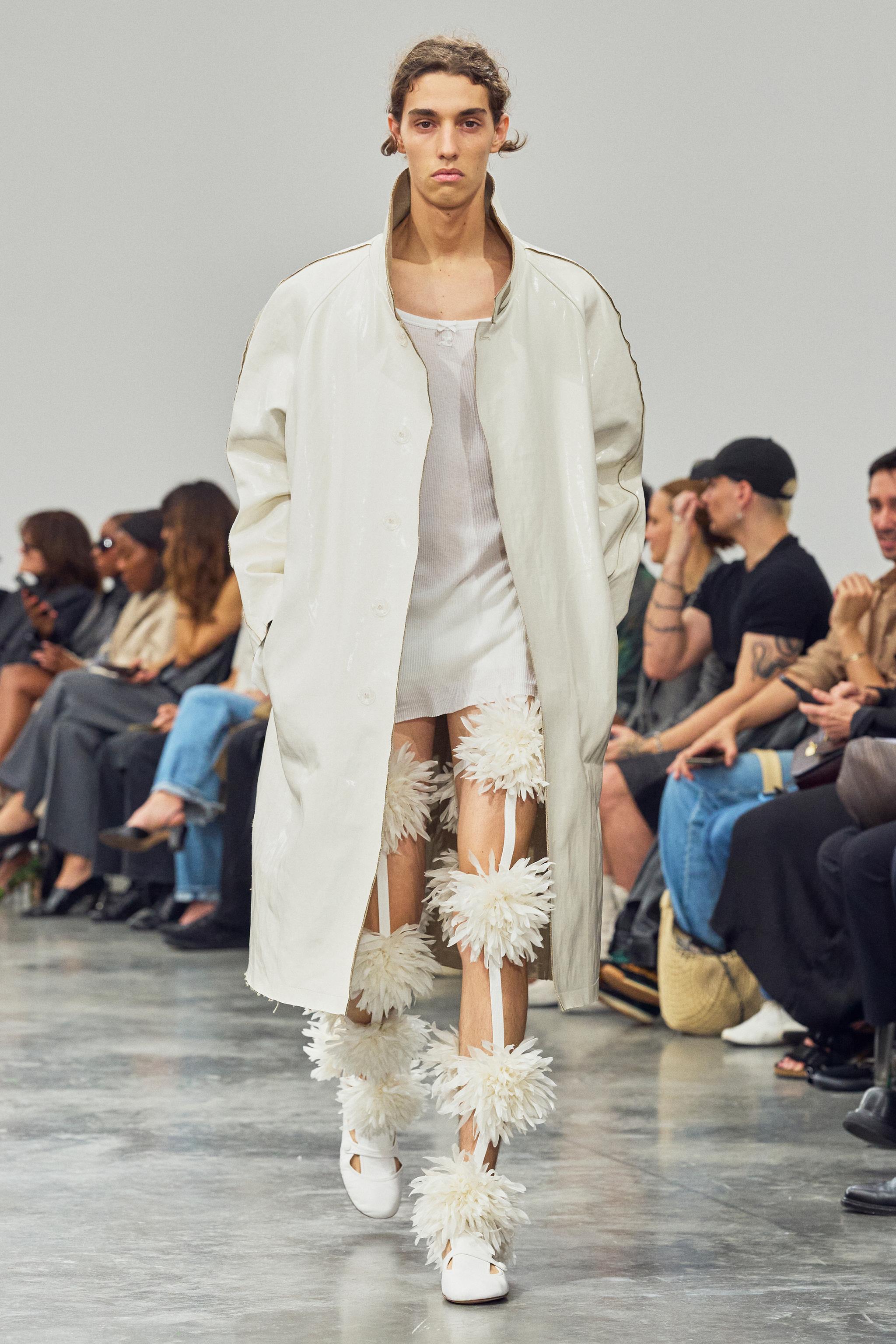 Ethereal runway look featuring a sleek white coat over delicate floral leg accessories for Courrèges.
