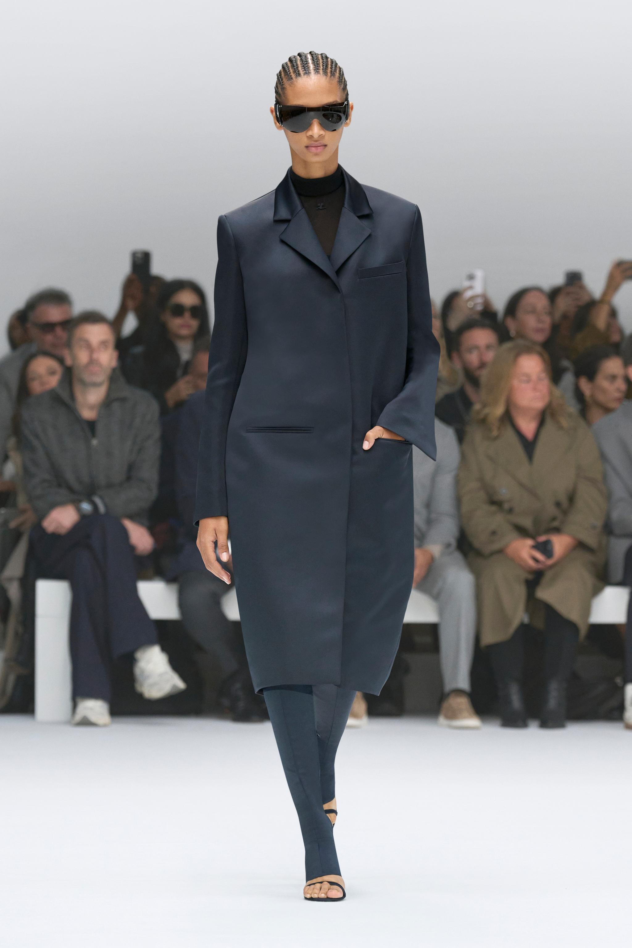 Elegant fashion-forward Courrèges model in a sleek navy coat and futuristic sunglasses.